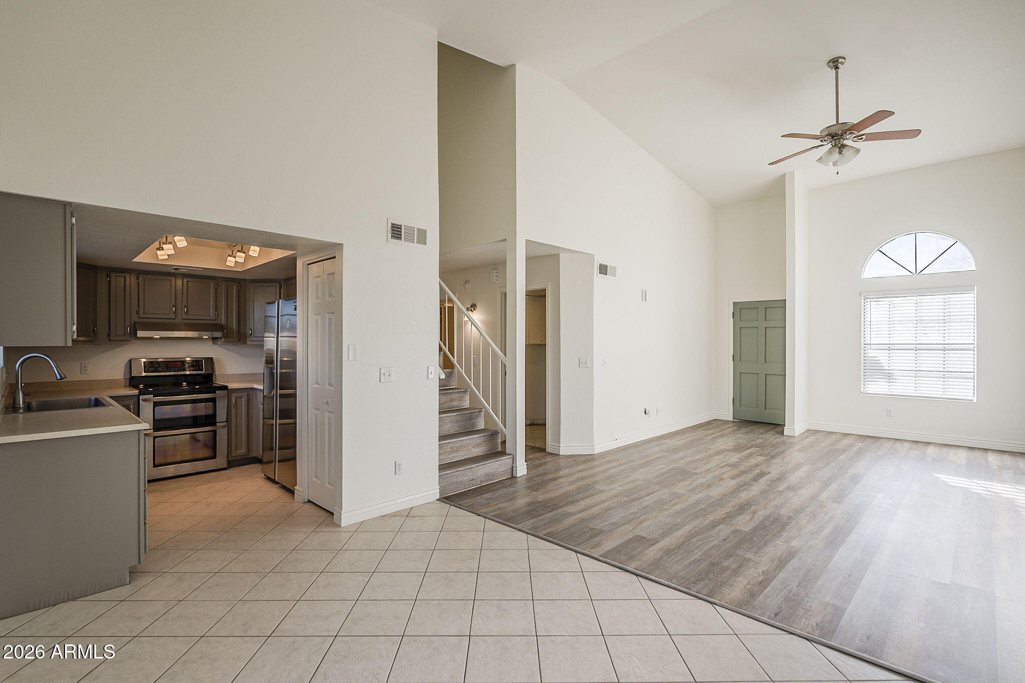 Open-plan kitchen and living room with dark cabinets, stainless steel appliances, and a staircase between them.