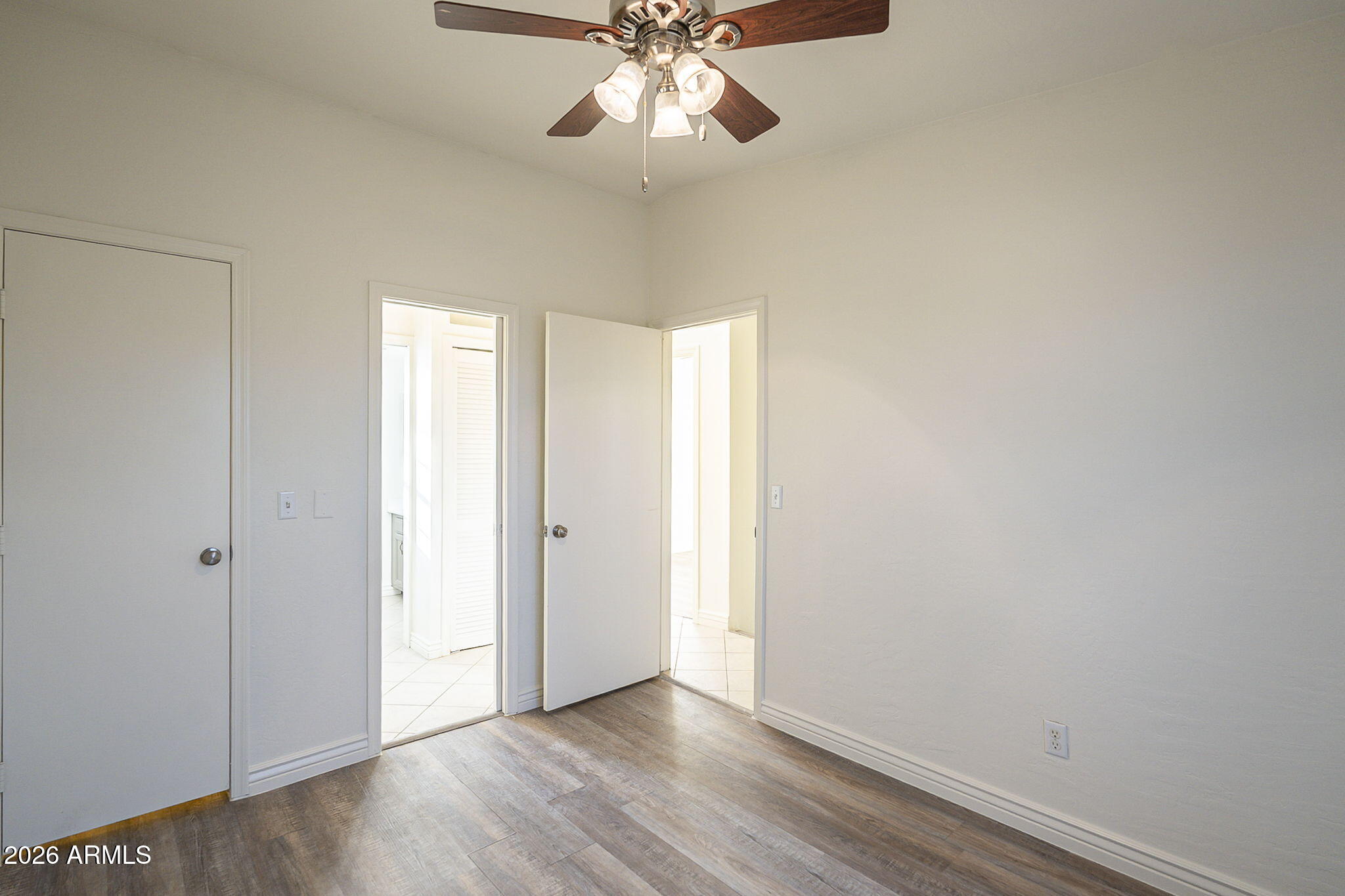 Empty bedroom with wood-look flooring, a ceiling fan, and open doorways.