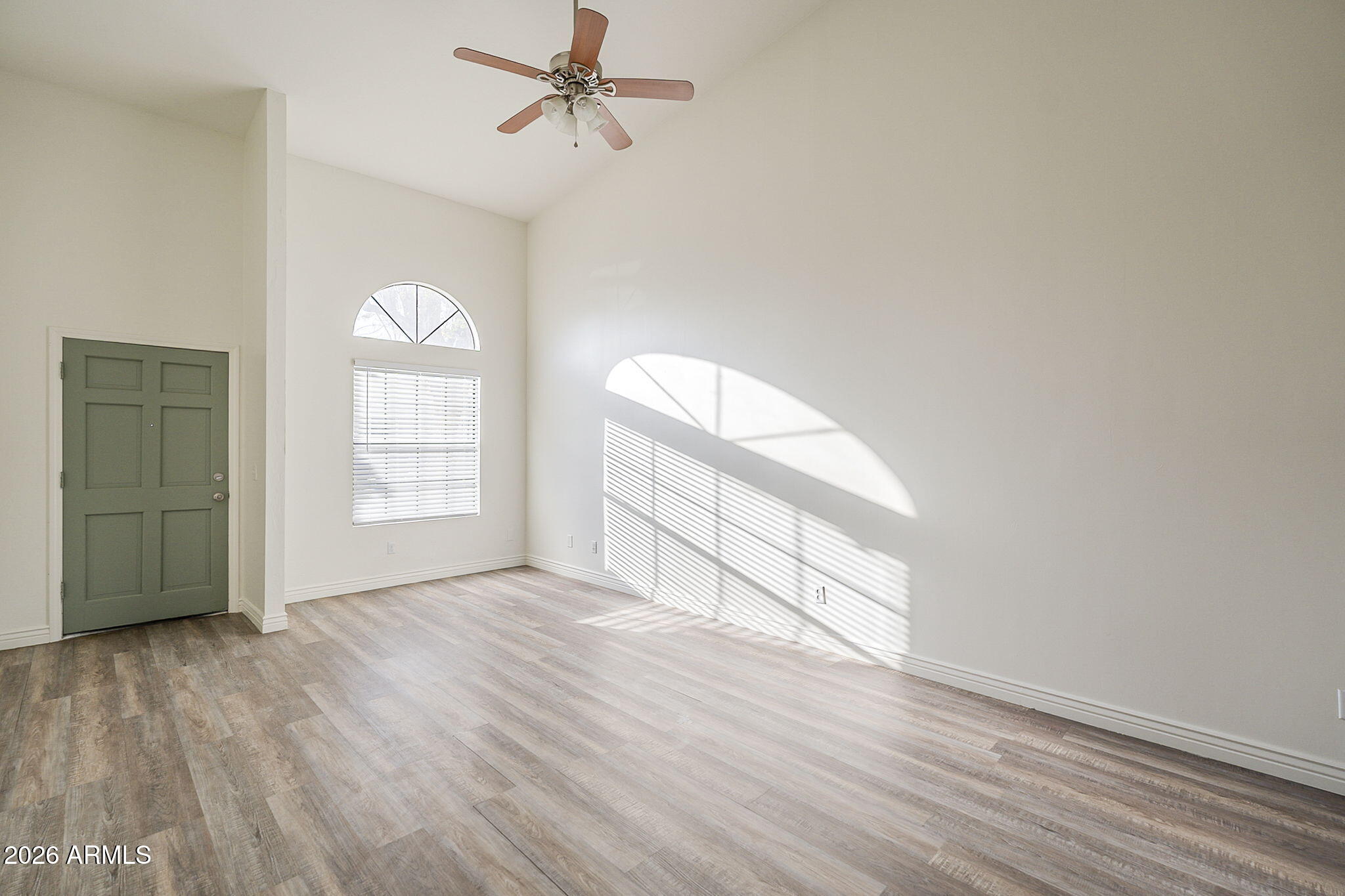 Vacant living room with high ceilings, wood-look flooring, and sunlight streaming through arched windows.