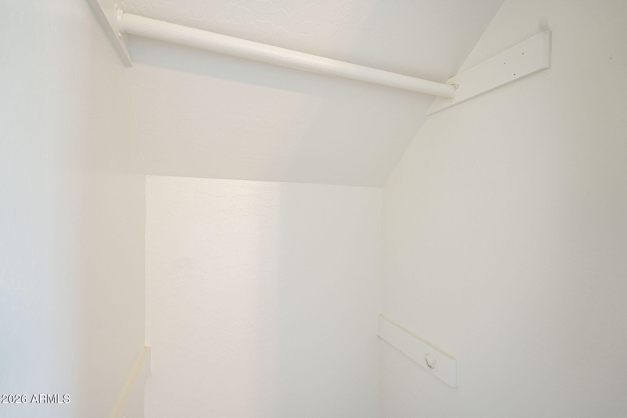 Small white interior space with wall-mounted rails beneath an angled ceiling.