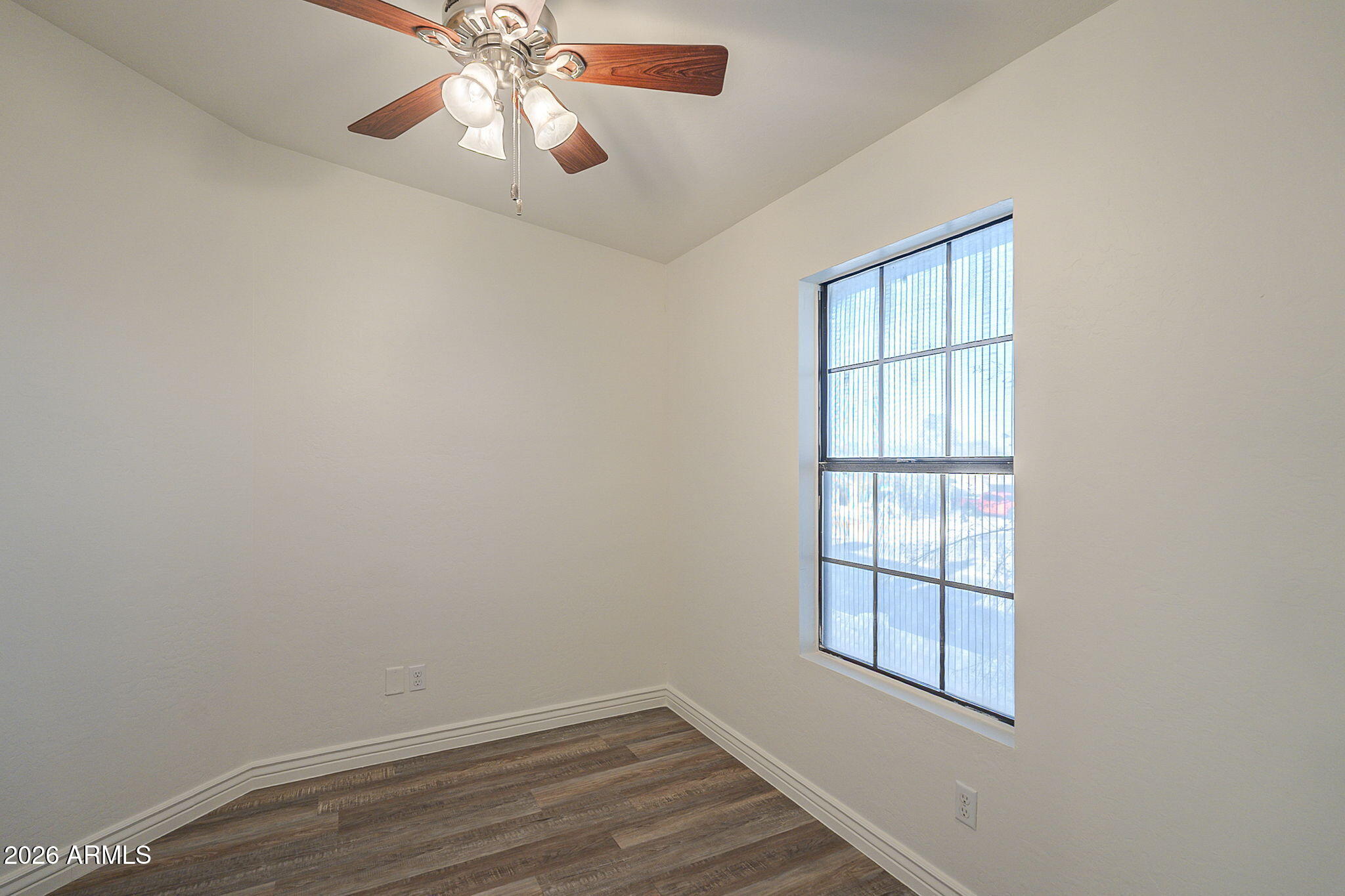 Empty room with dark wood-look flooring, a tall window with vertical blinds, and a ceiling fan.