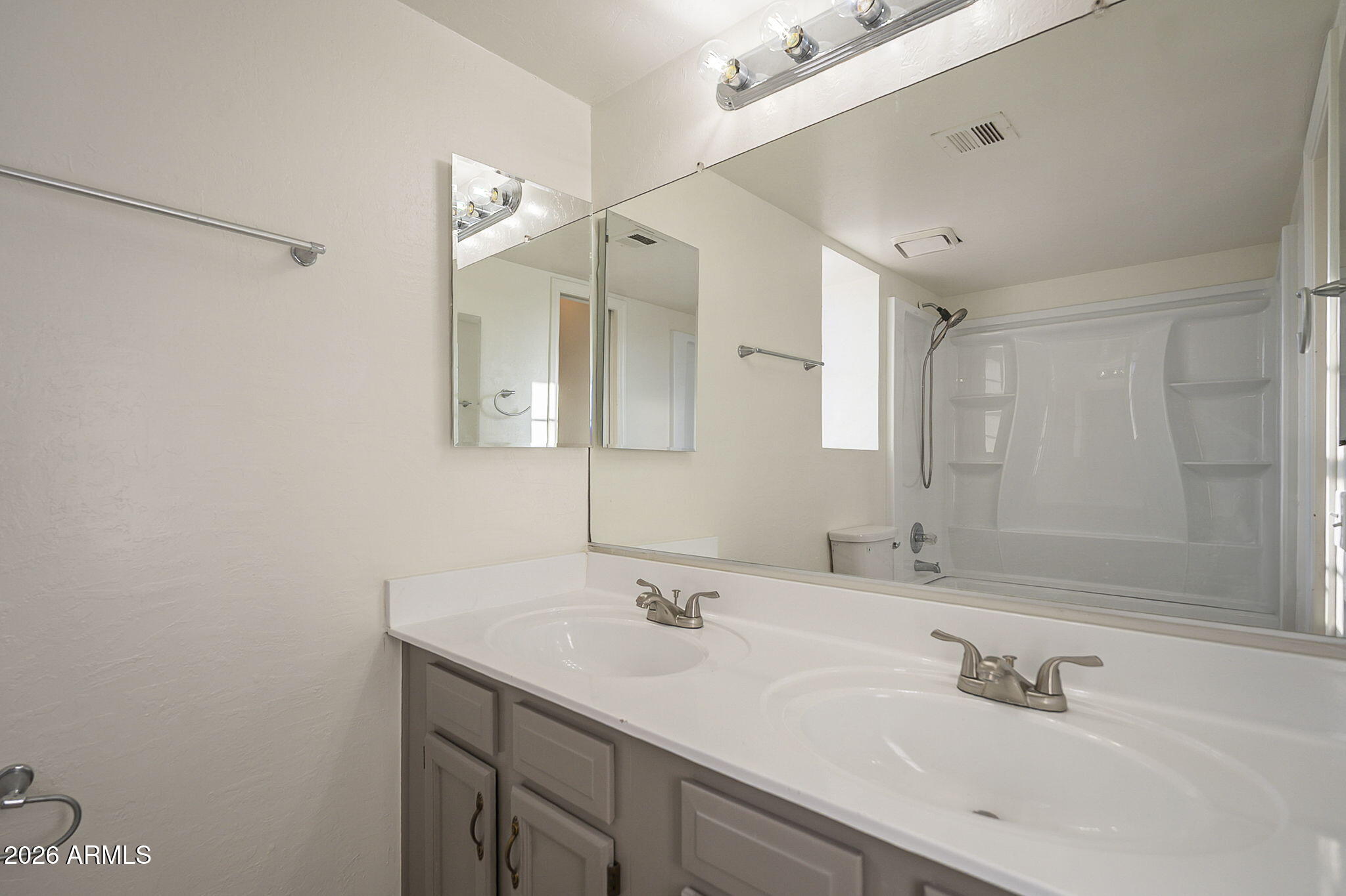 Bathroom with double-sink vanity and large mirror facing a white tub-shower surround.