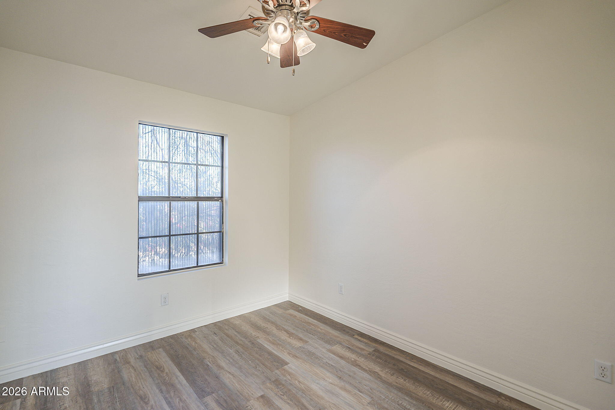 Empty bedroom with wood-look flooring, a window with vertical blinds, and a ceiling fan.