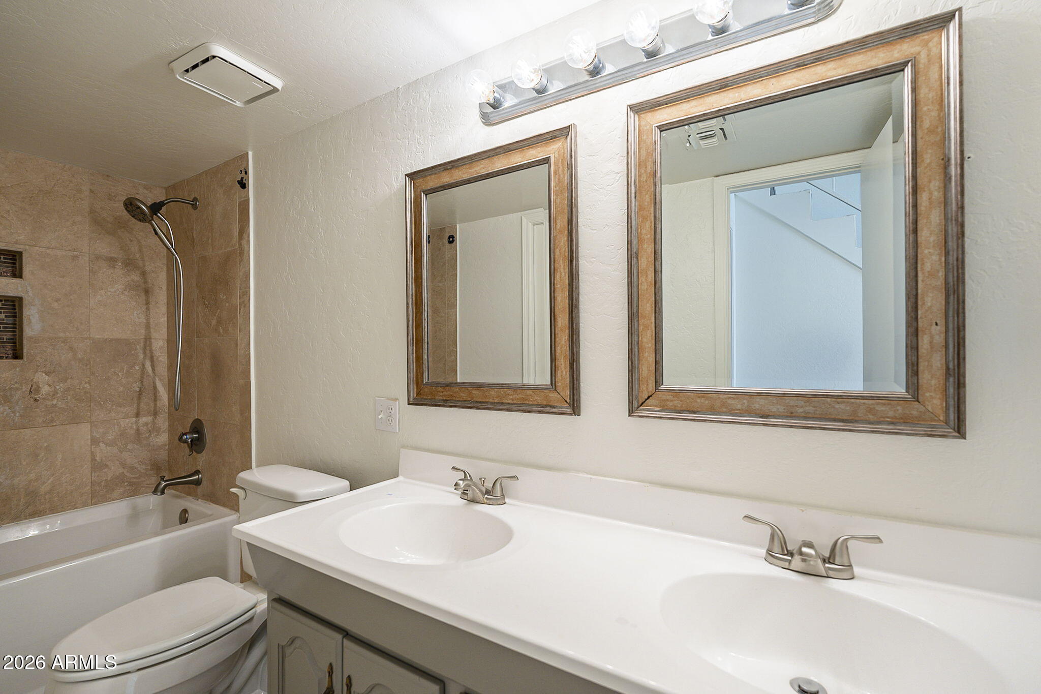 Bathroom with a double vanity, two framed mirrors, and a tiled tub-shower surround.