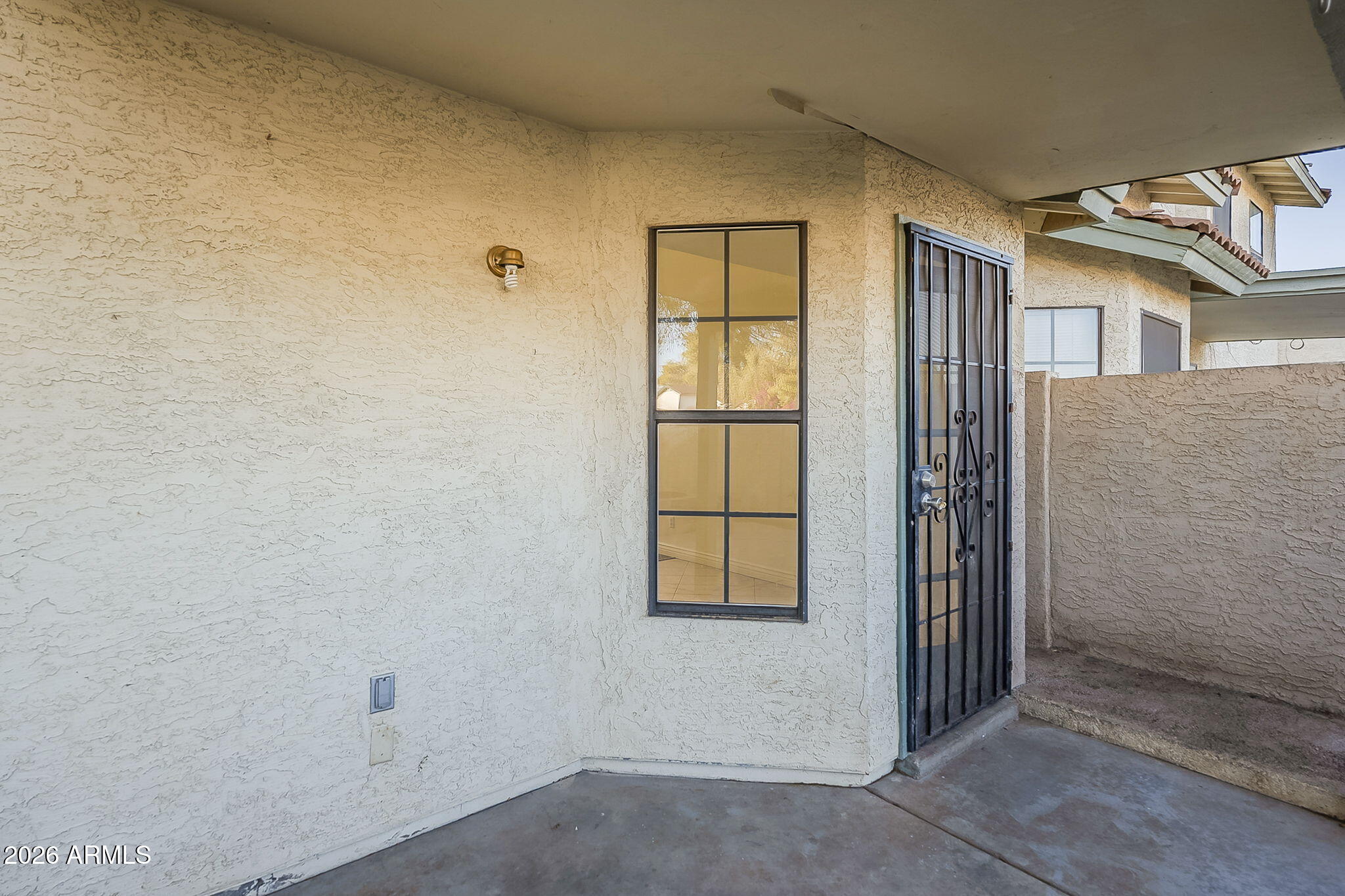 Covered stucco entry porch with a divided-pane window and black security screen door.