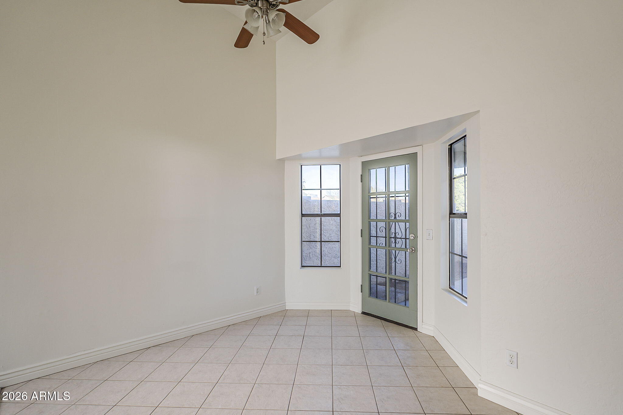 Empty tiled entry room with a green glass-paneled door, narrow windows, and a ceiling fan.