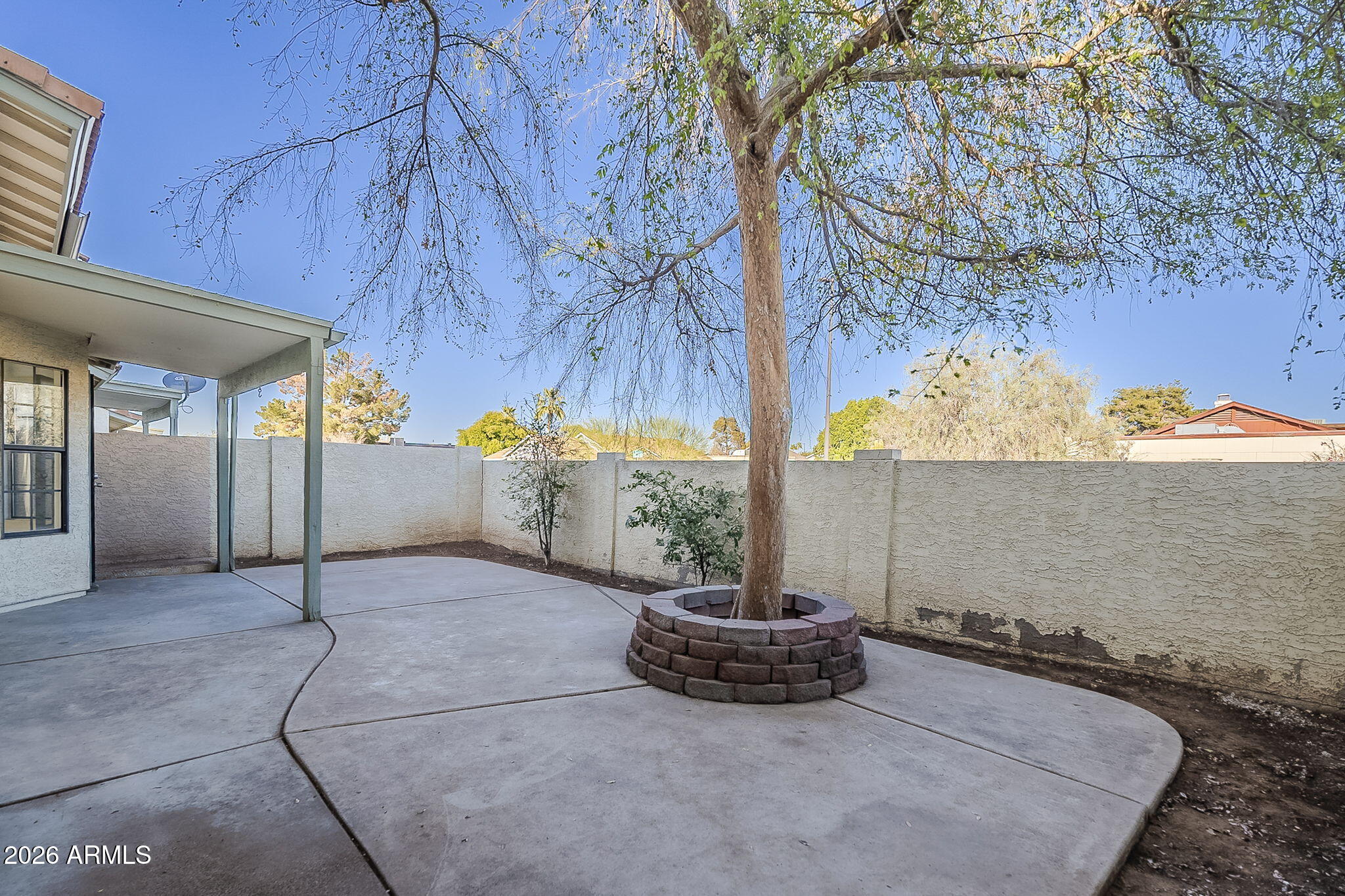 Backyard patio with a covered section and a mature tree in a circular block planter.