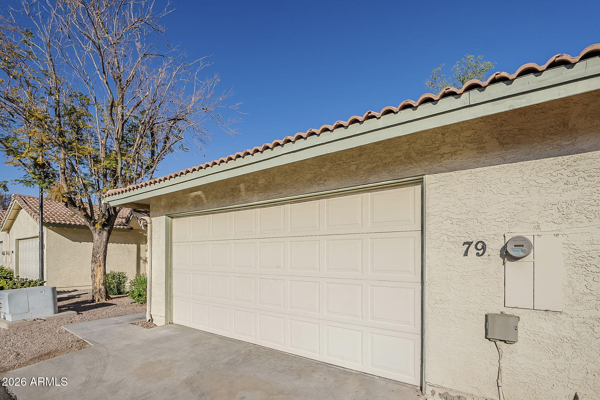 Home exterior with a large paneled garage door, tiled roof, and the number 79 beside the meter.