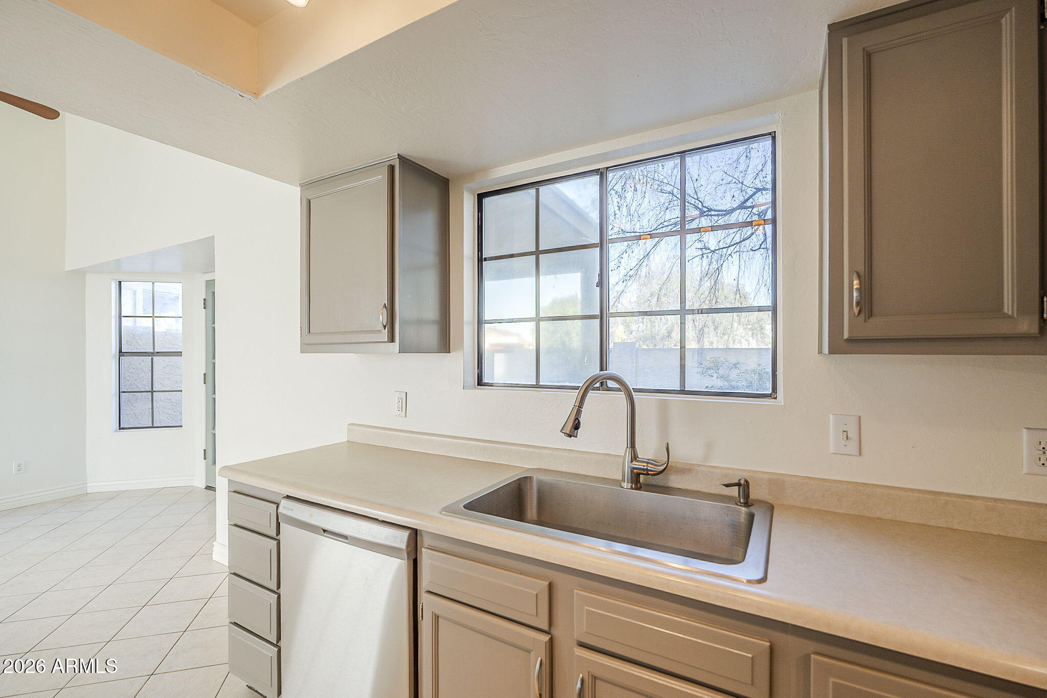 Kitchen with taupe cabinets, a stainless steel sink beneath a large window, and a dishwasher.