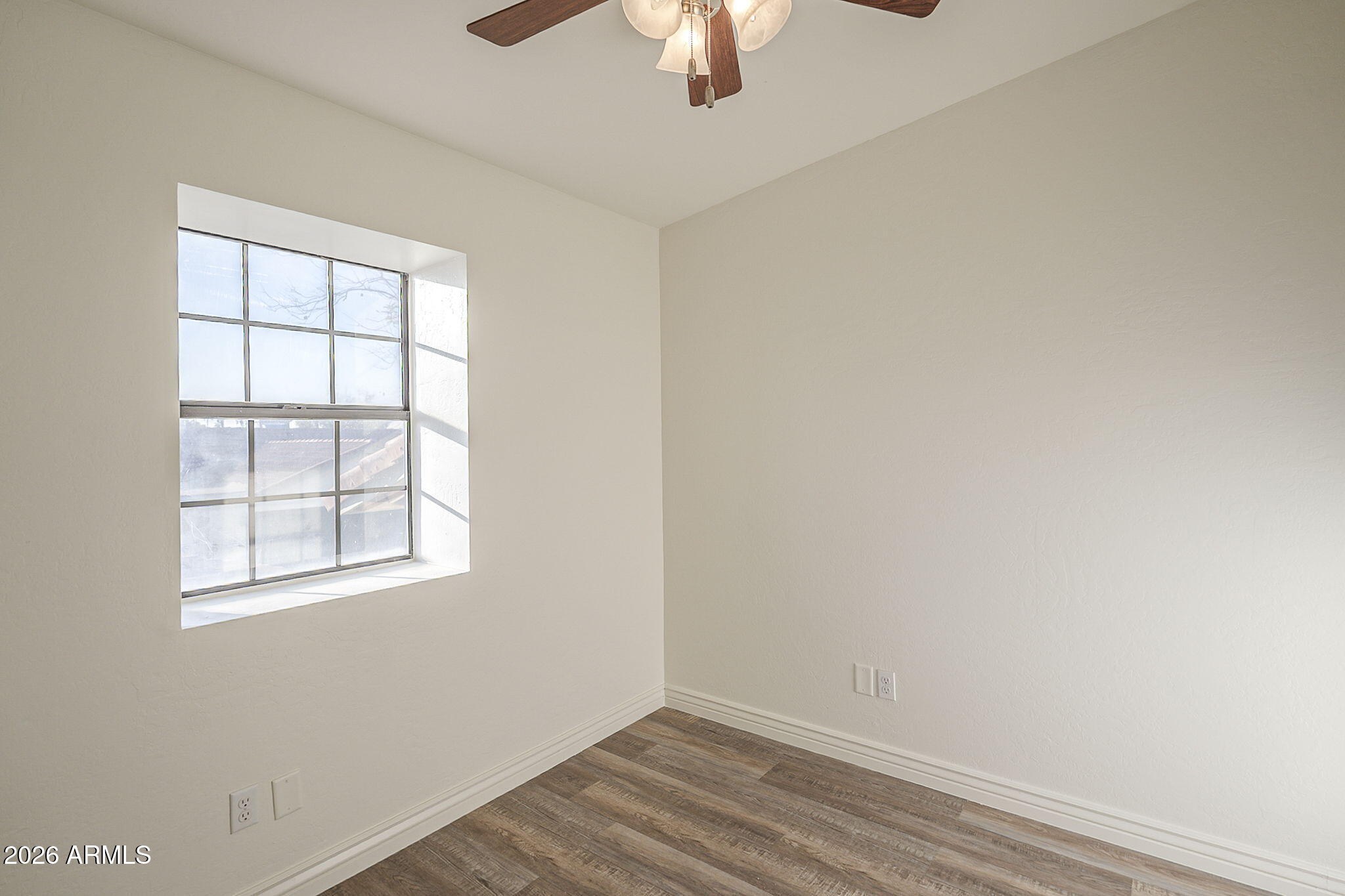 Empty room with wood-look flooring, a large grid-pane window, and a ceiling fan.