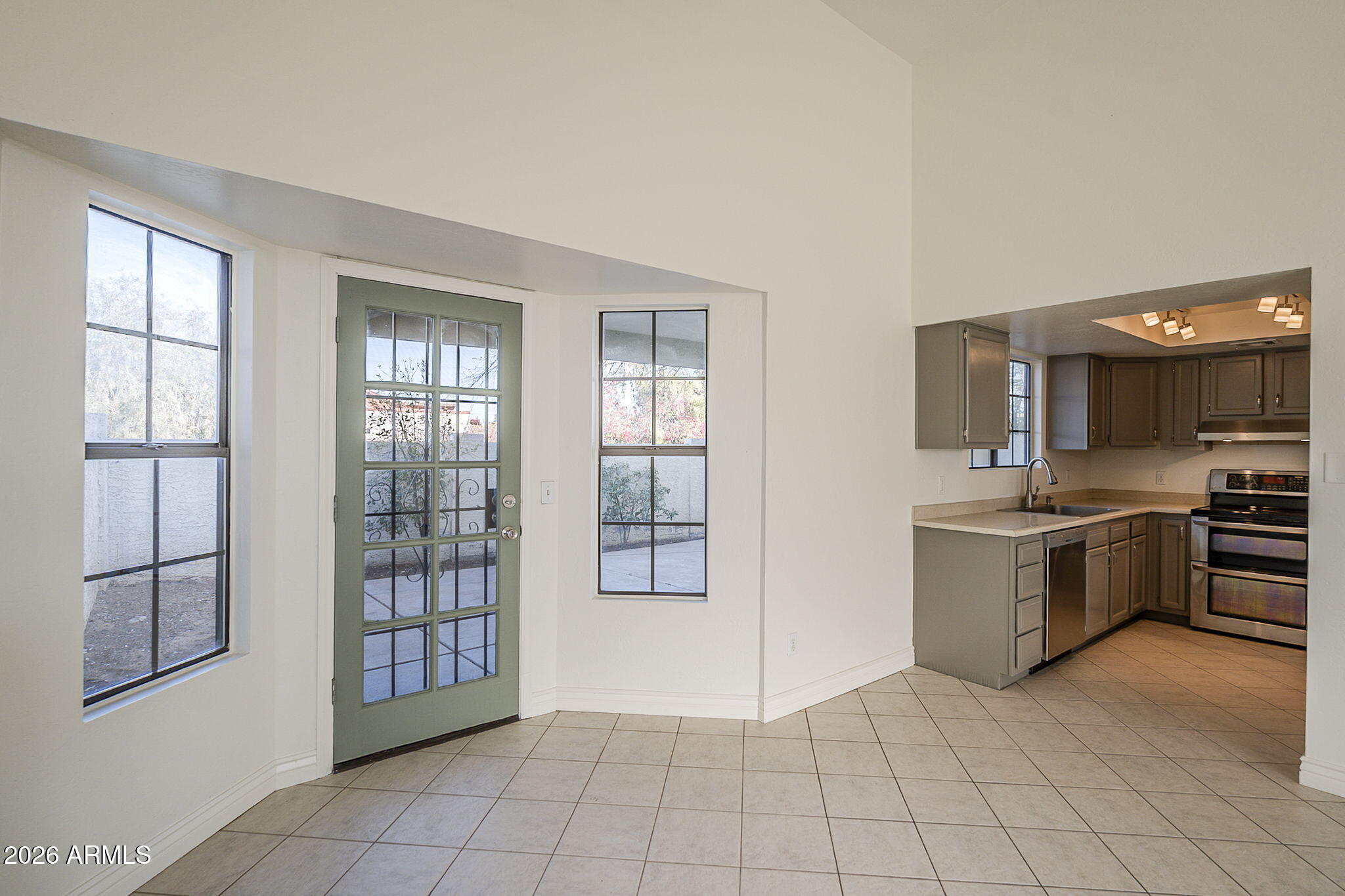 Kitchen and tiled entry with a green glass-paneled door, windows, dark cabinets, and stainless steel appliances.