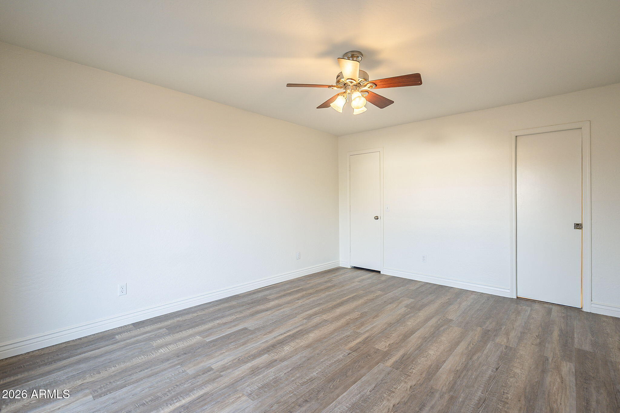 Empty room with wood-look plank flooring and a lit ceiling fan with wooden blades.