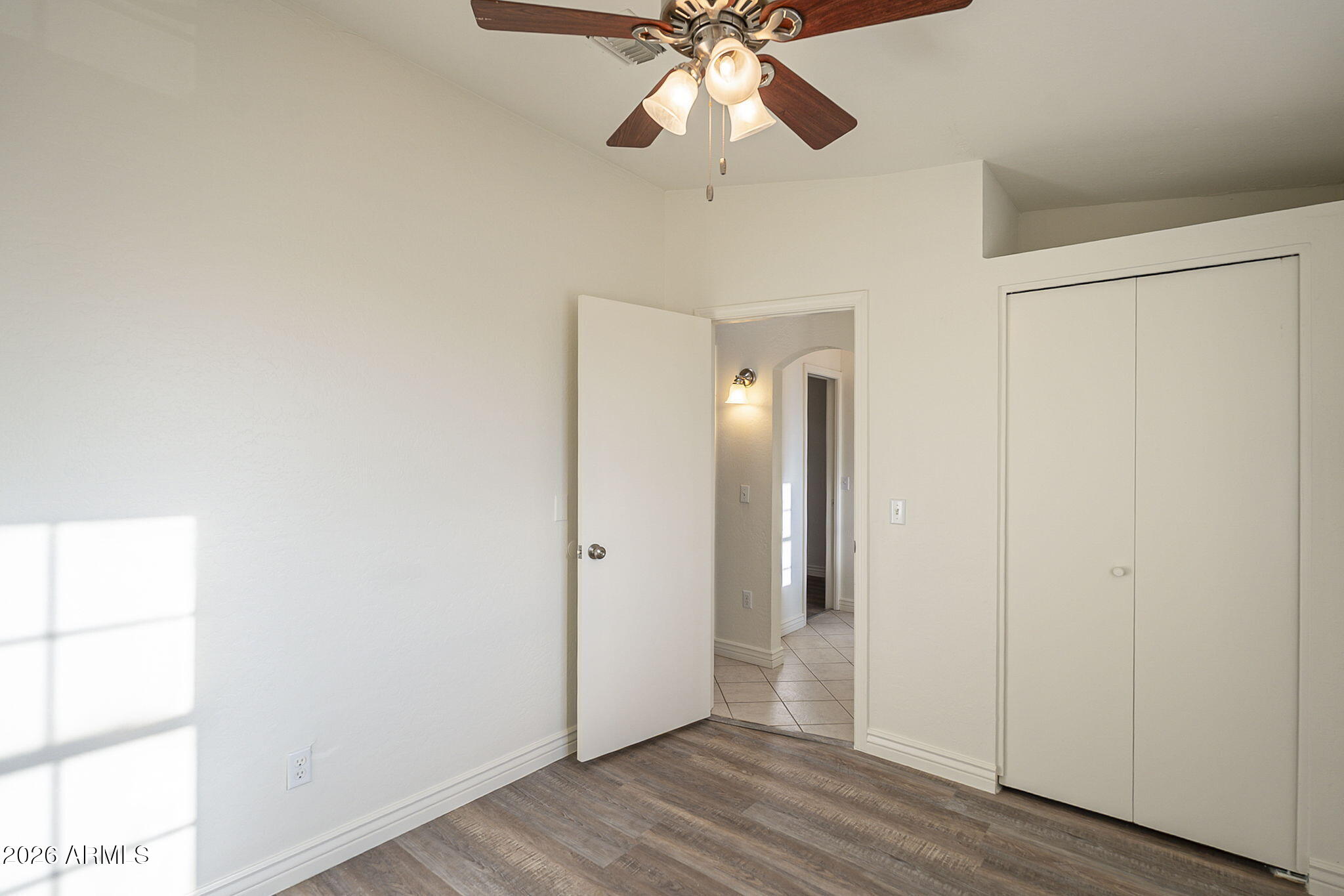 Empty bedroom with a ceiling fan, sliding-door closet, and wood-look flooring.