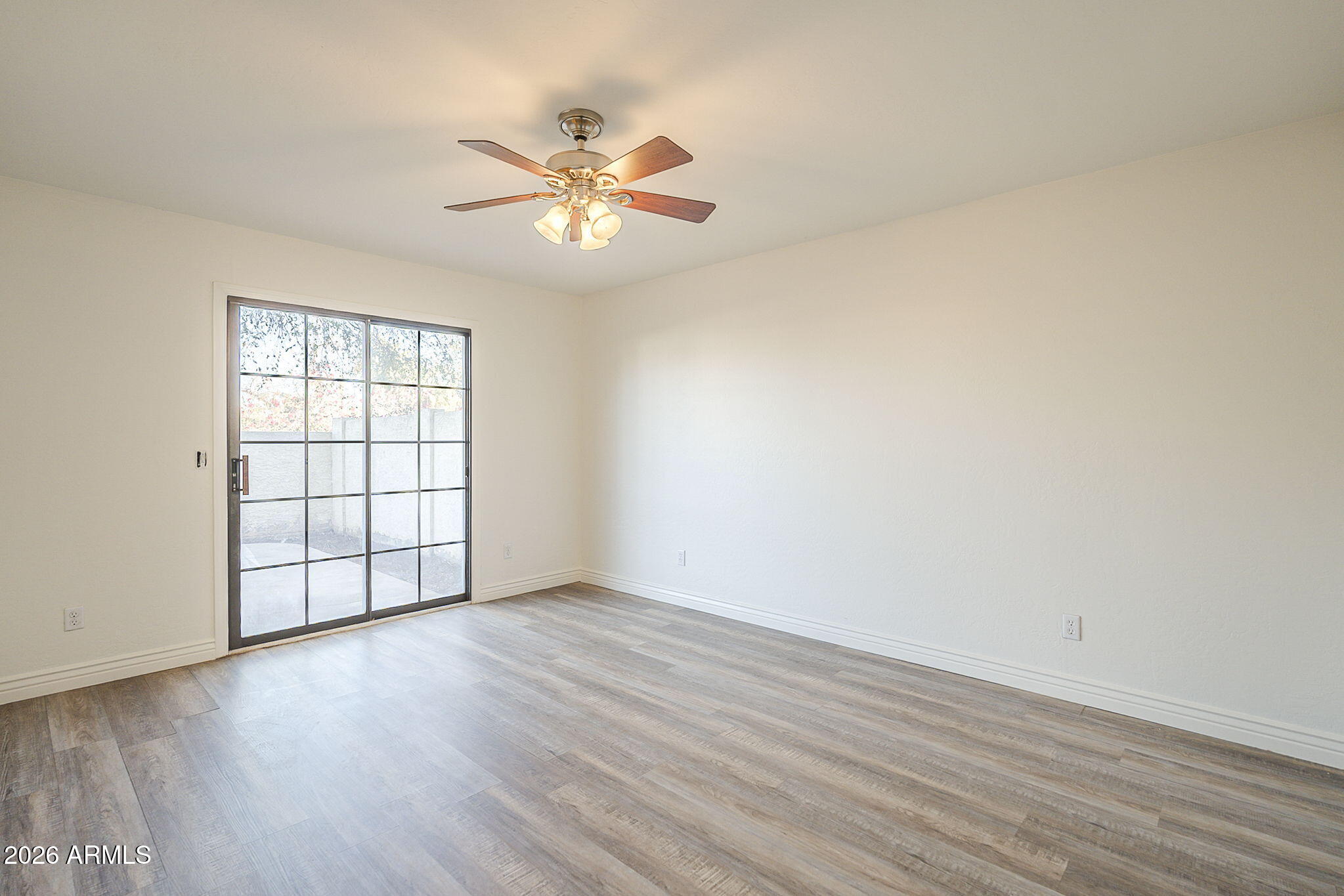 Empty room with gray wood-look flooring, ceiling fan, and black-framed sliding glass door.