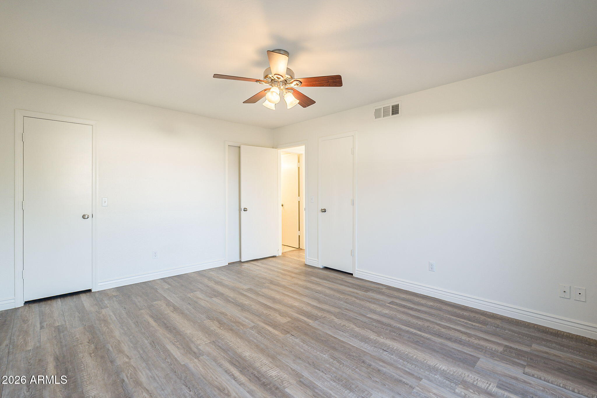 Empty bedroom with gray plank flooring and a ceiling fan with lights.