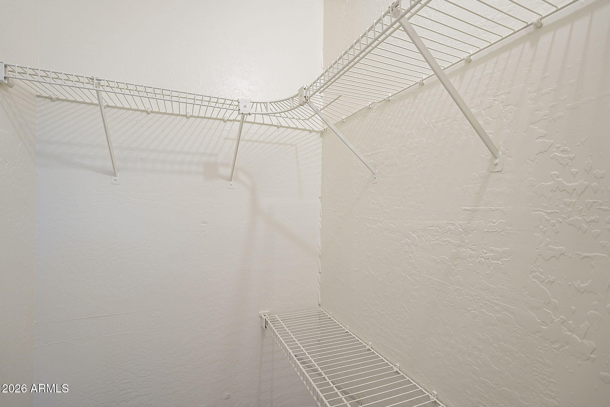 Empty walk-in closet with white wire shelving wrapping around the walls.