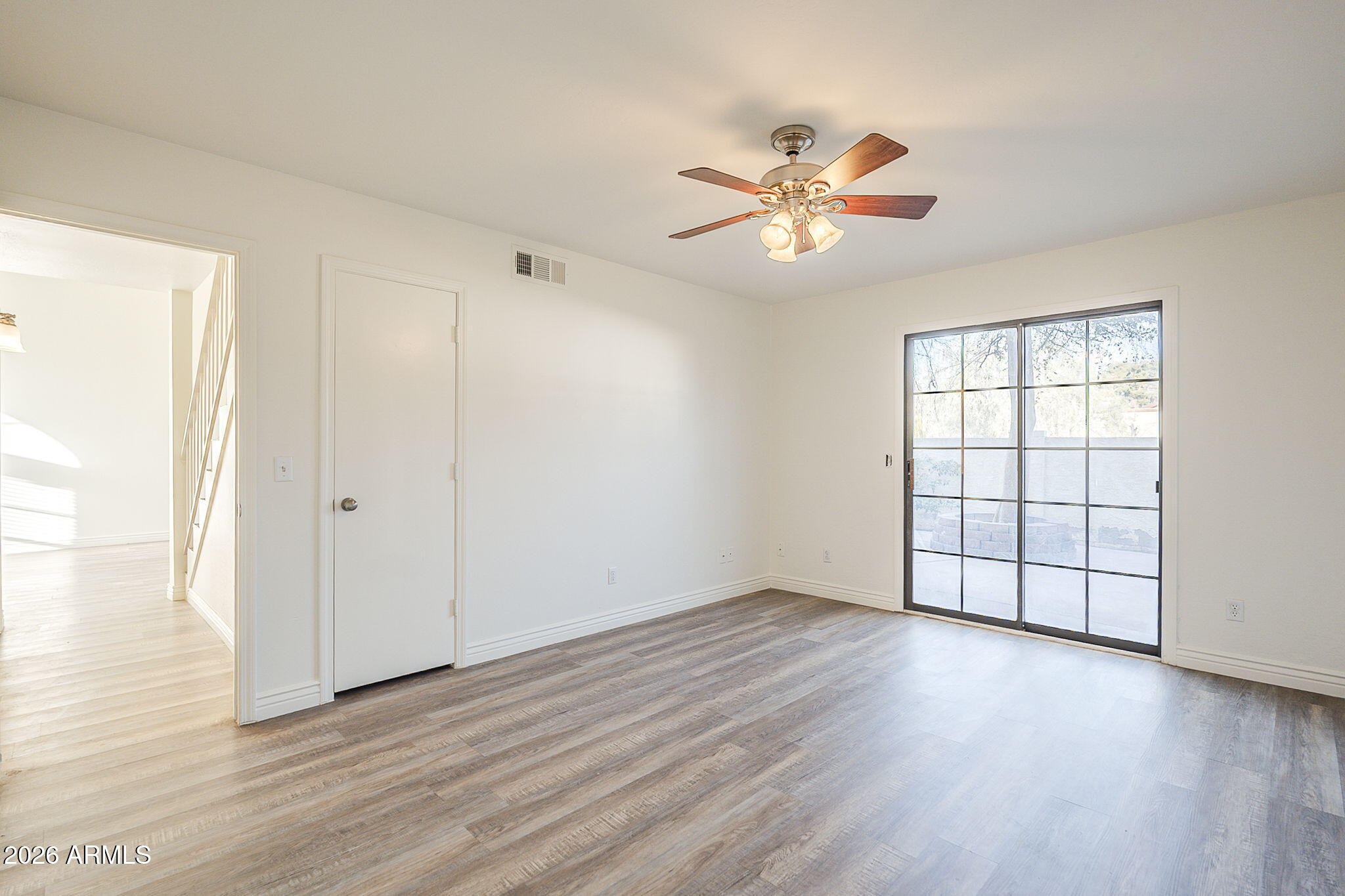 Vacant room with plank flooring, a ceiling fan, and a black-grid sliding glass door to the patio.