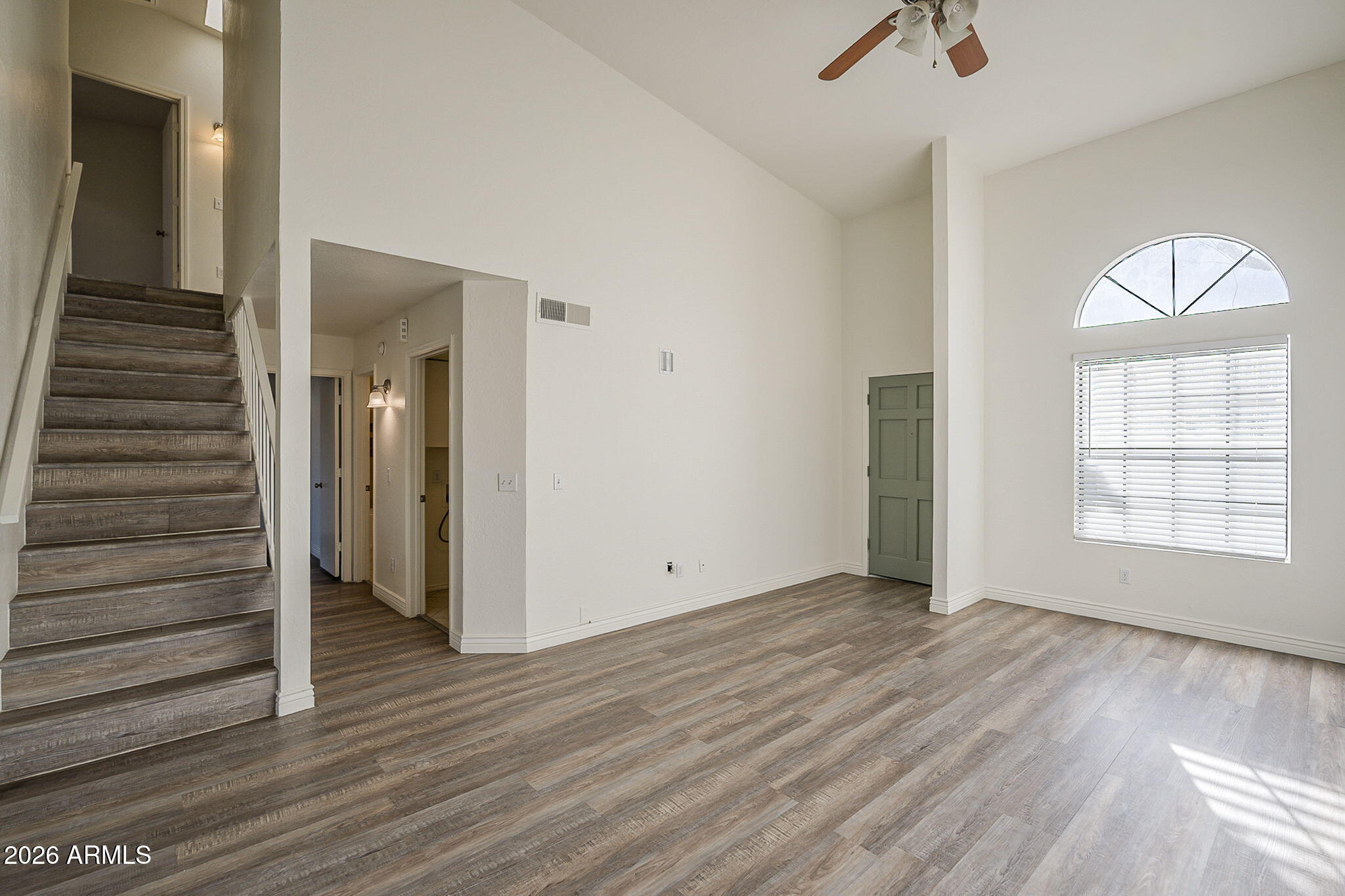 Vacant living area with a tall arched window, wood-look floors, and staircase.