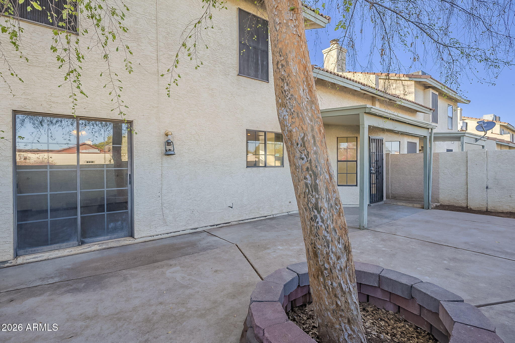 Townhouse rear patio with a covered entry, sliding glass door, and mature tree in a circular planter.