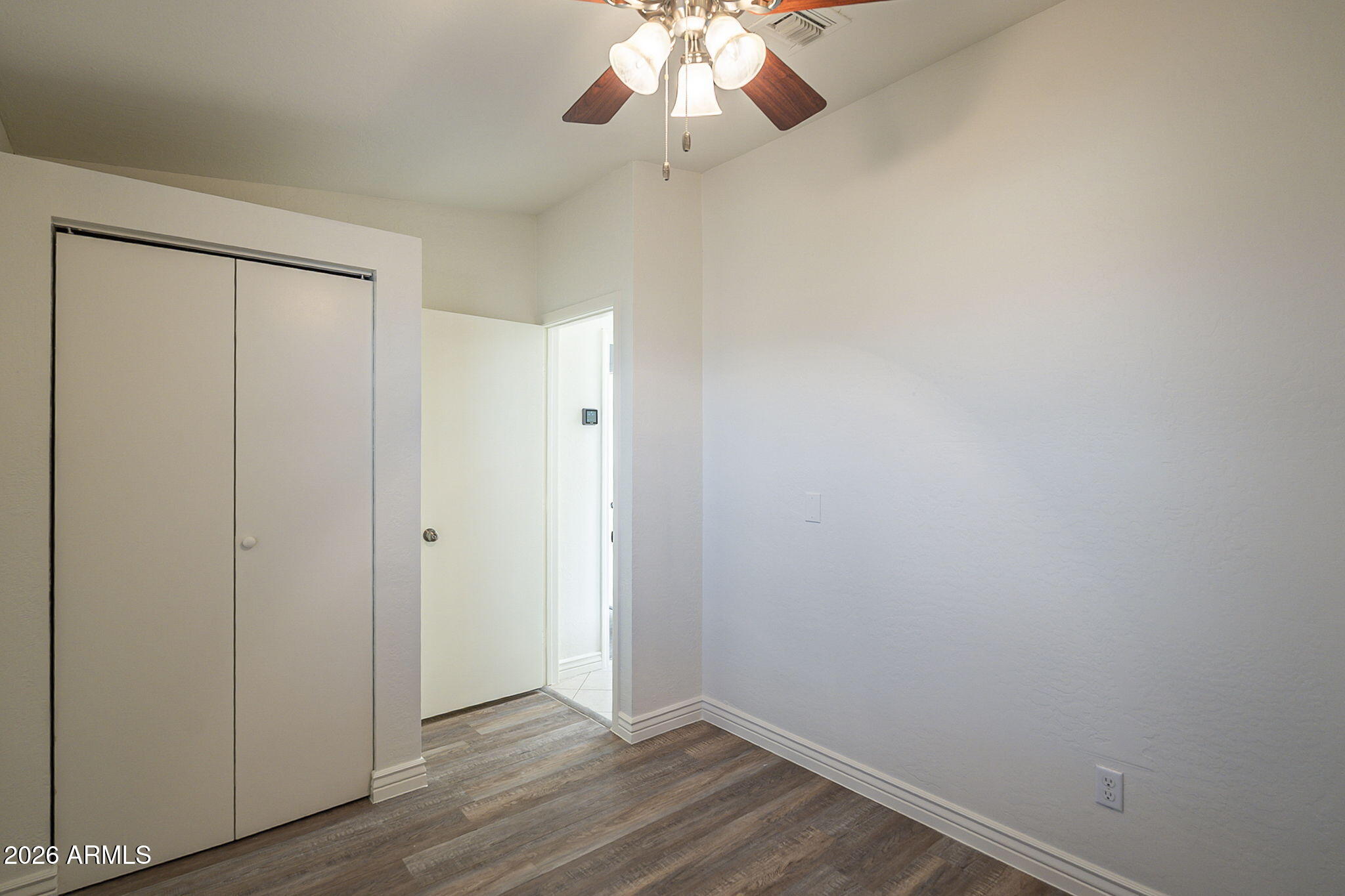 Empty bedroom with sliding closet doors, wood-look flooring, and a ceiling fan.