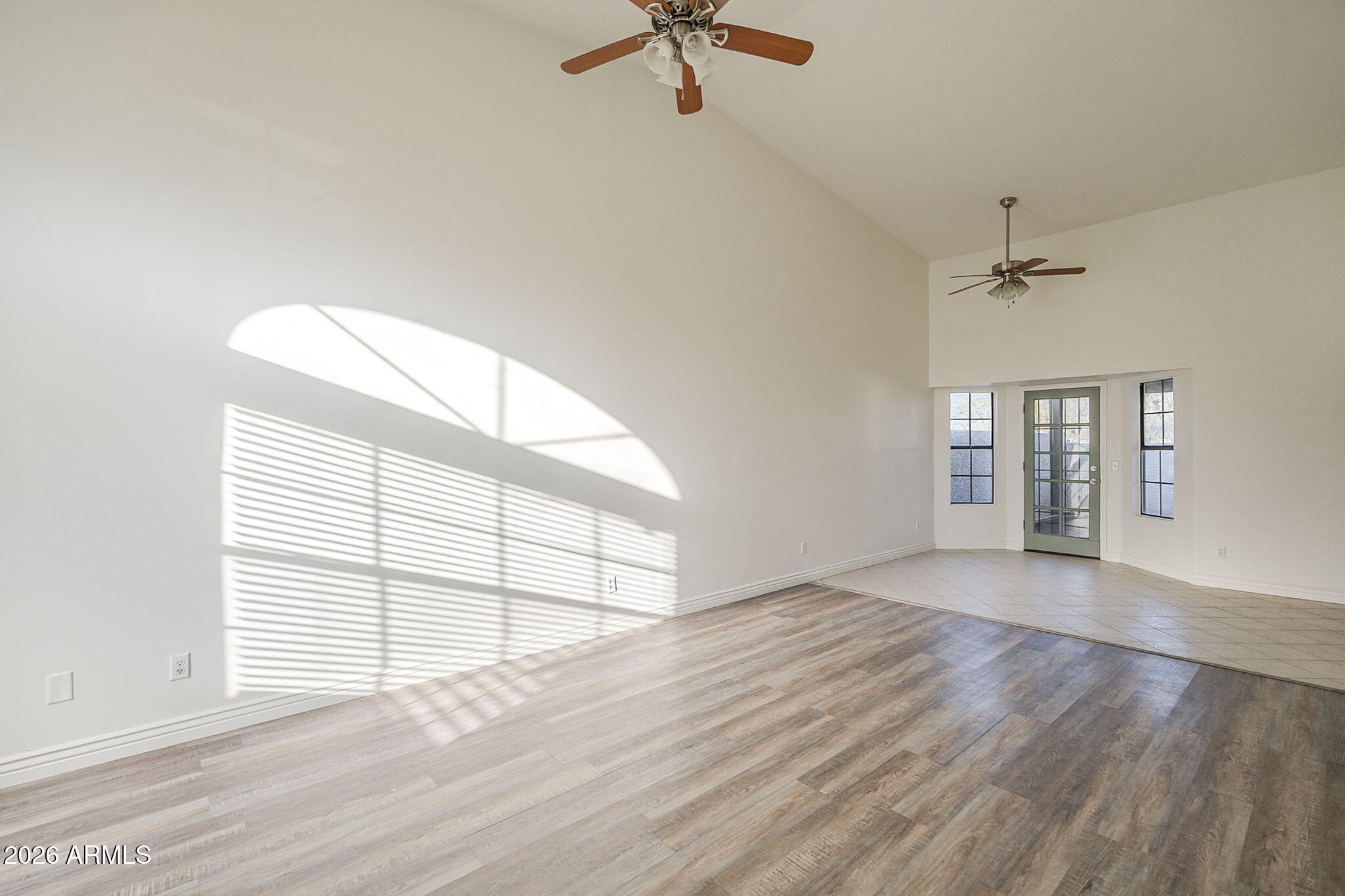 Vacant living room with vaulted ceiling, wood-look floors, and sunlight streaming through windows.