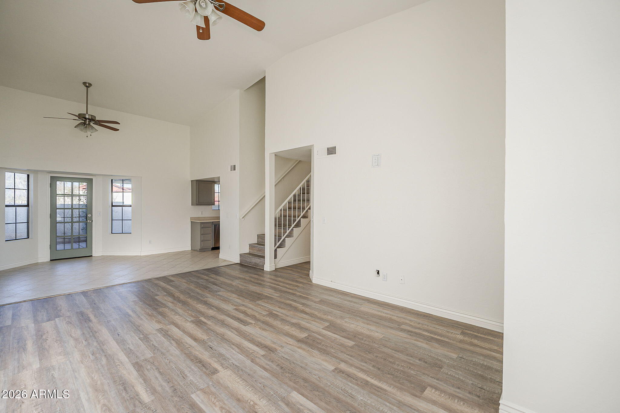 Empty living area with wood-look flooring, two ceiling fans, and a staircase.