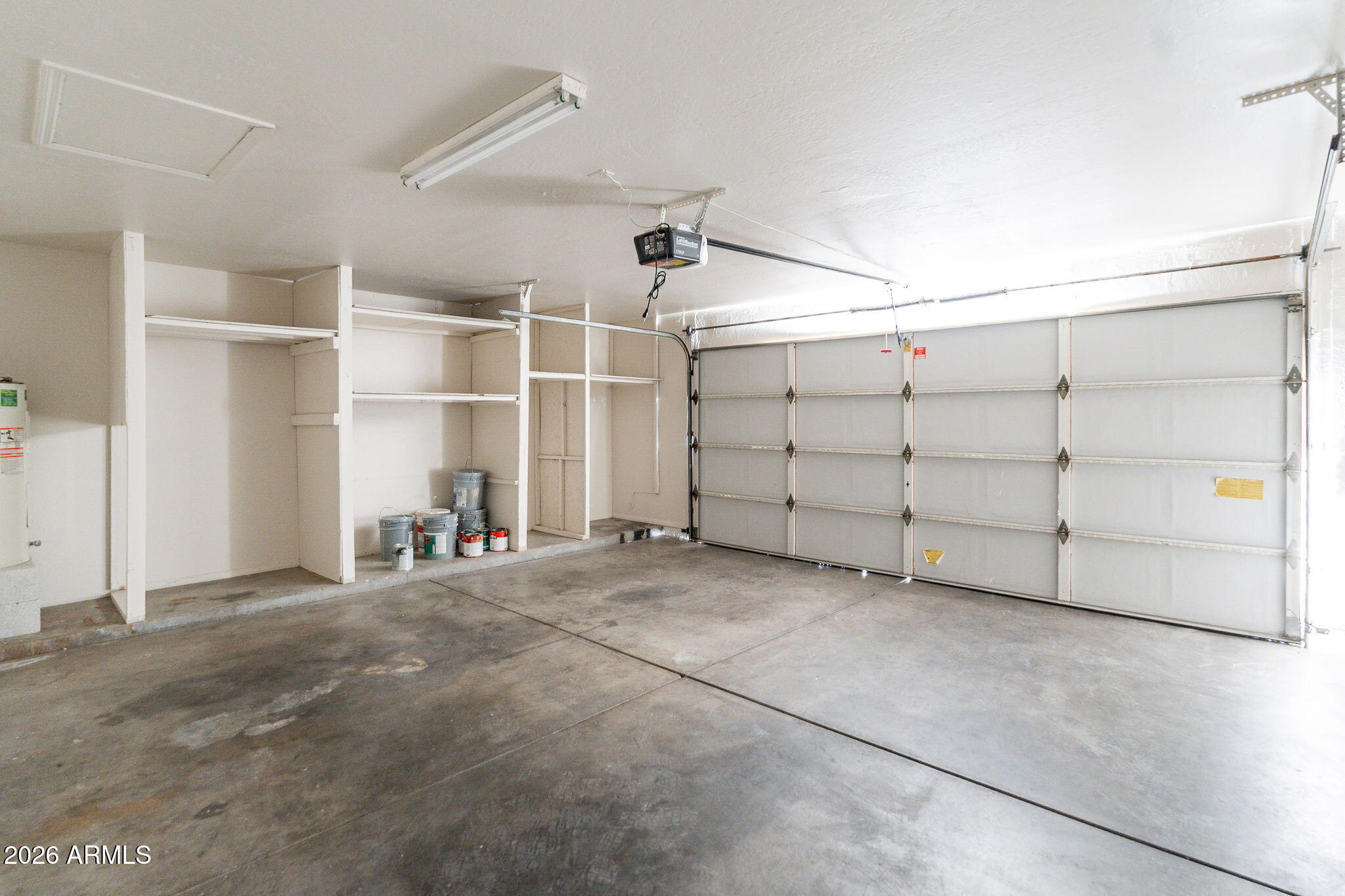 Empty garage with built-in storage shelves, paint buckets, and a large sectional garage door.
