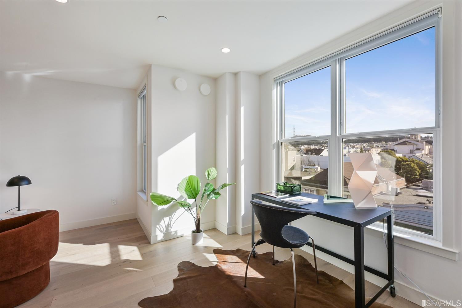Bright office with a black desk beside large windows overlooking city rooftops.