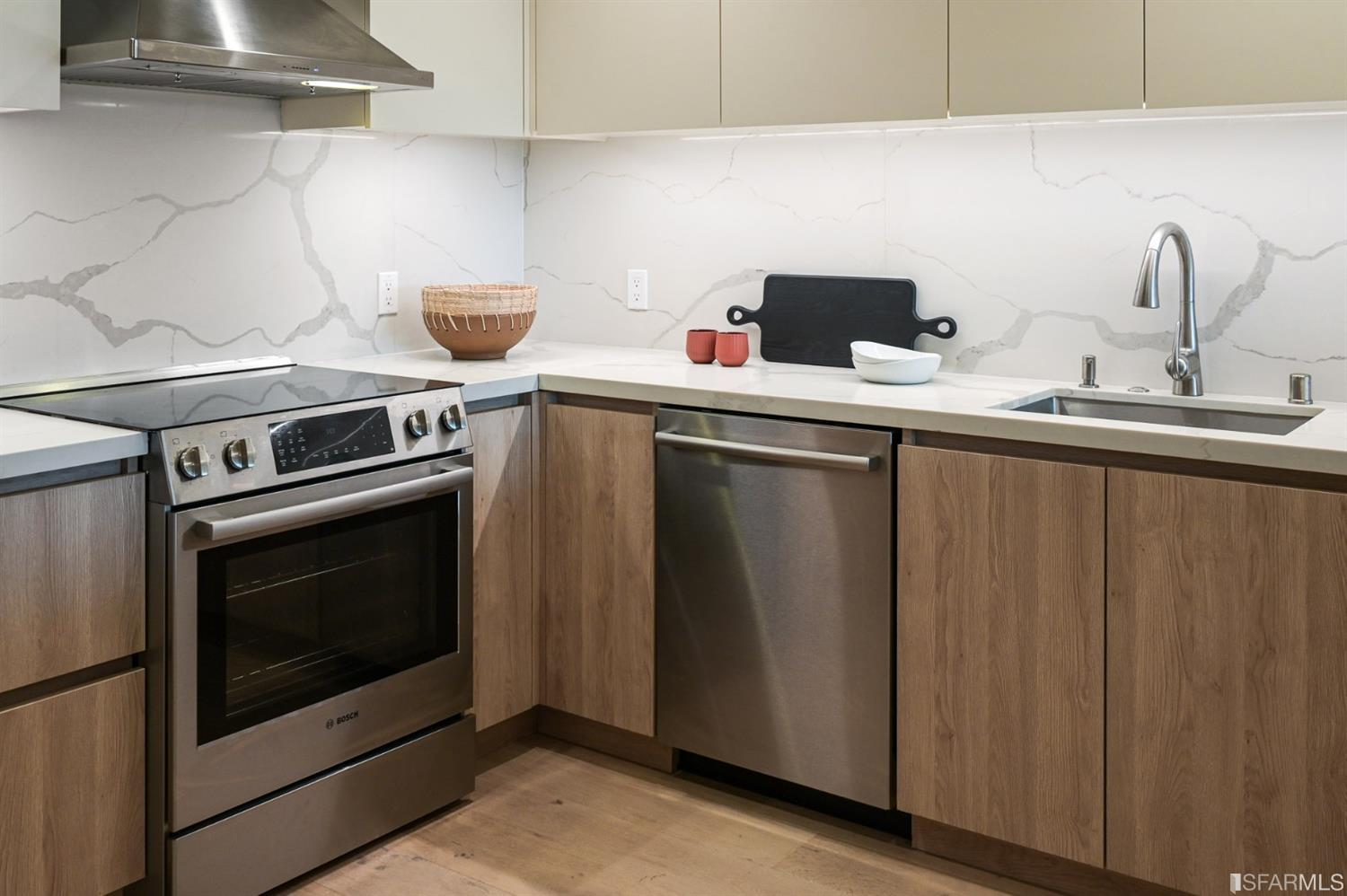 Modern kitchen with wood-grain cabinets, veined stone backsplash, stainless steel appliances, and a single-basin sink.