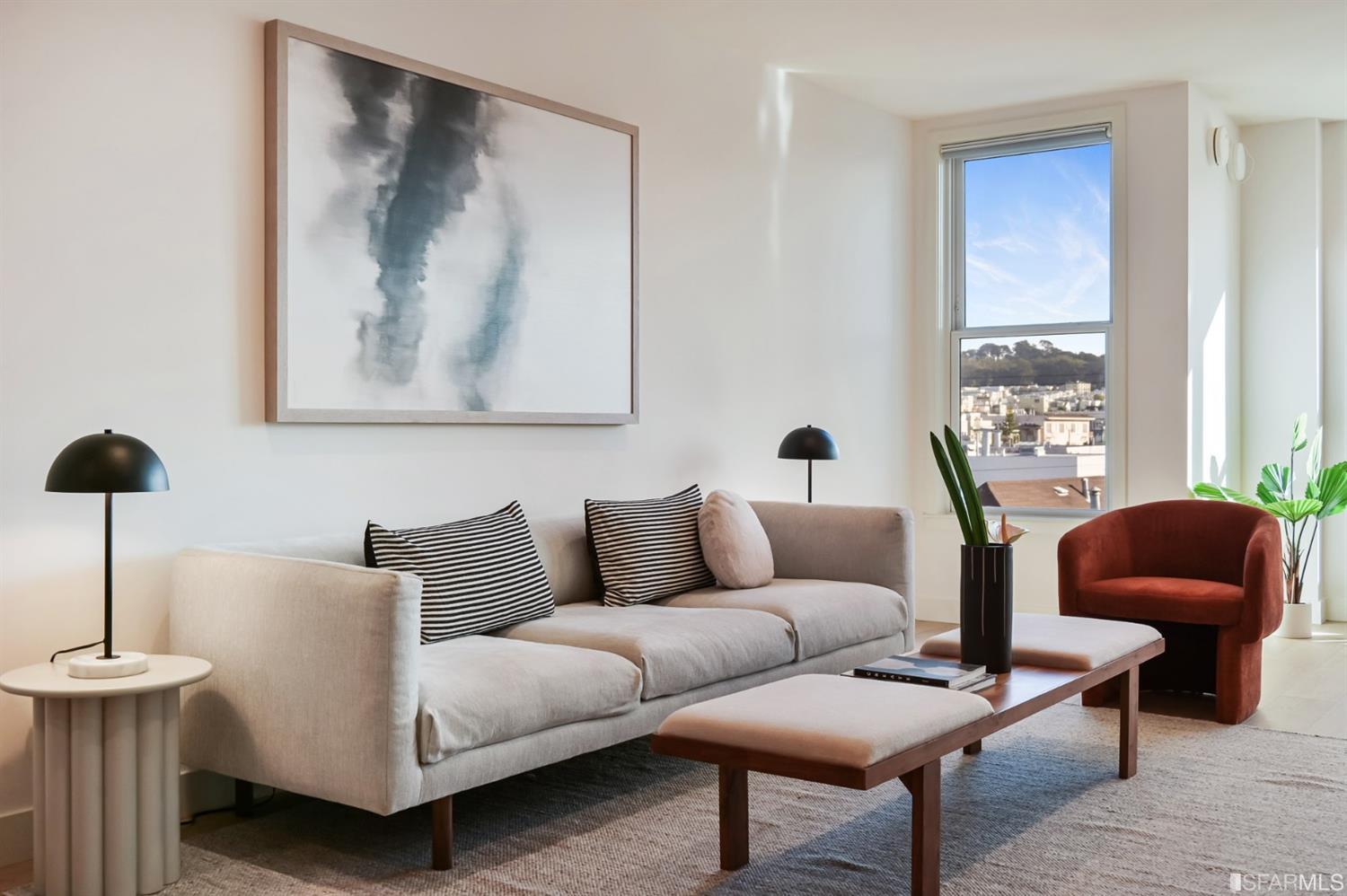 Staged living room with a light sofa and rust-colored armchair beside a large window.