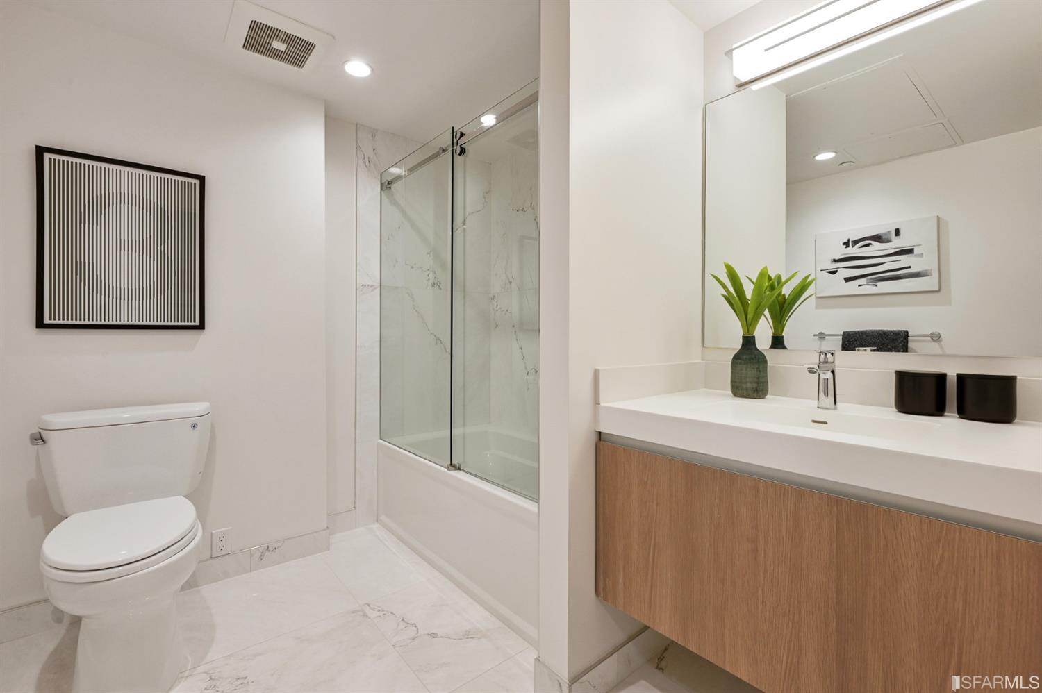 Modern bathroom with a glass-enclosed tub and shower, marble-look tile, and a wood-front vanity.