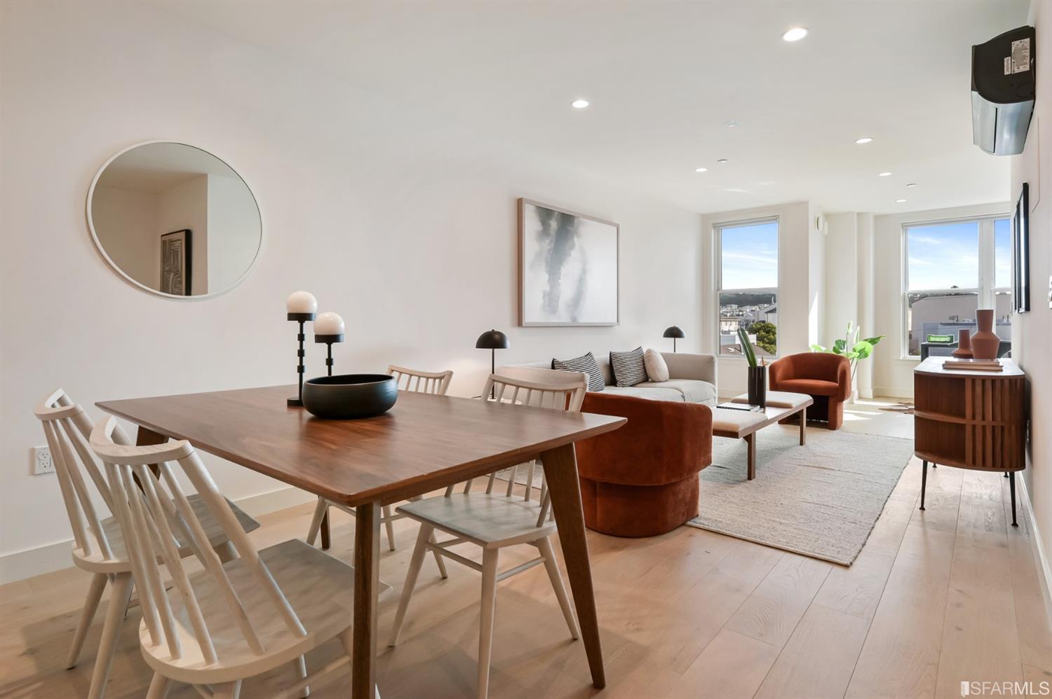 Staged dining and living area with a wooden table, rust-colored chairs, and large city-facing windows.