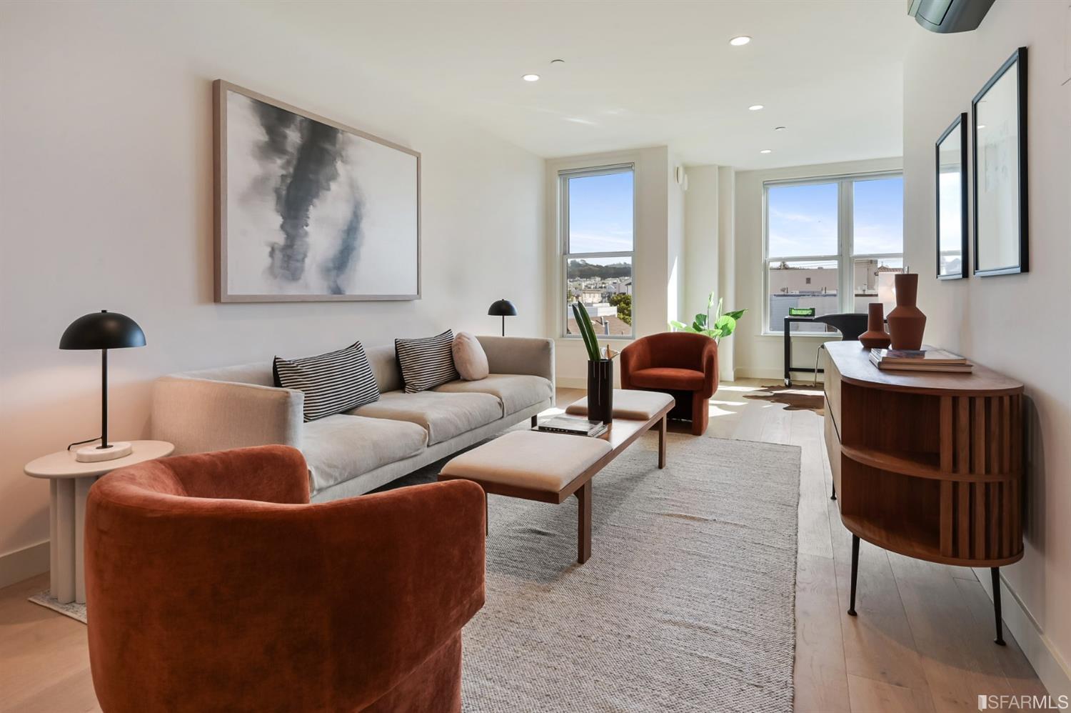 Staged living room with rust-colored armchairs, a gray sofa, and tall sunlit windows.