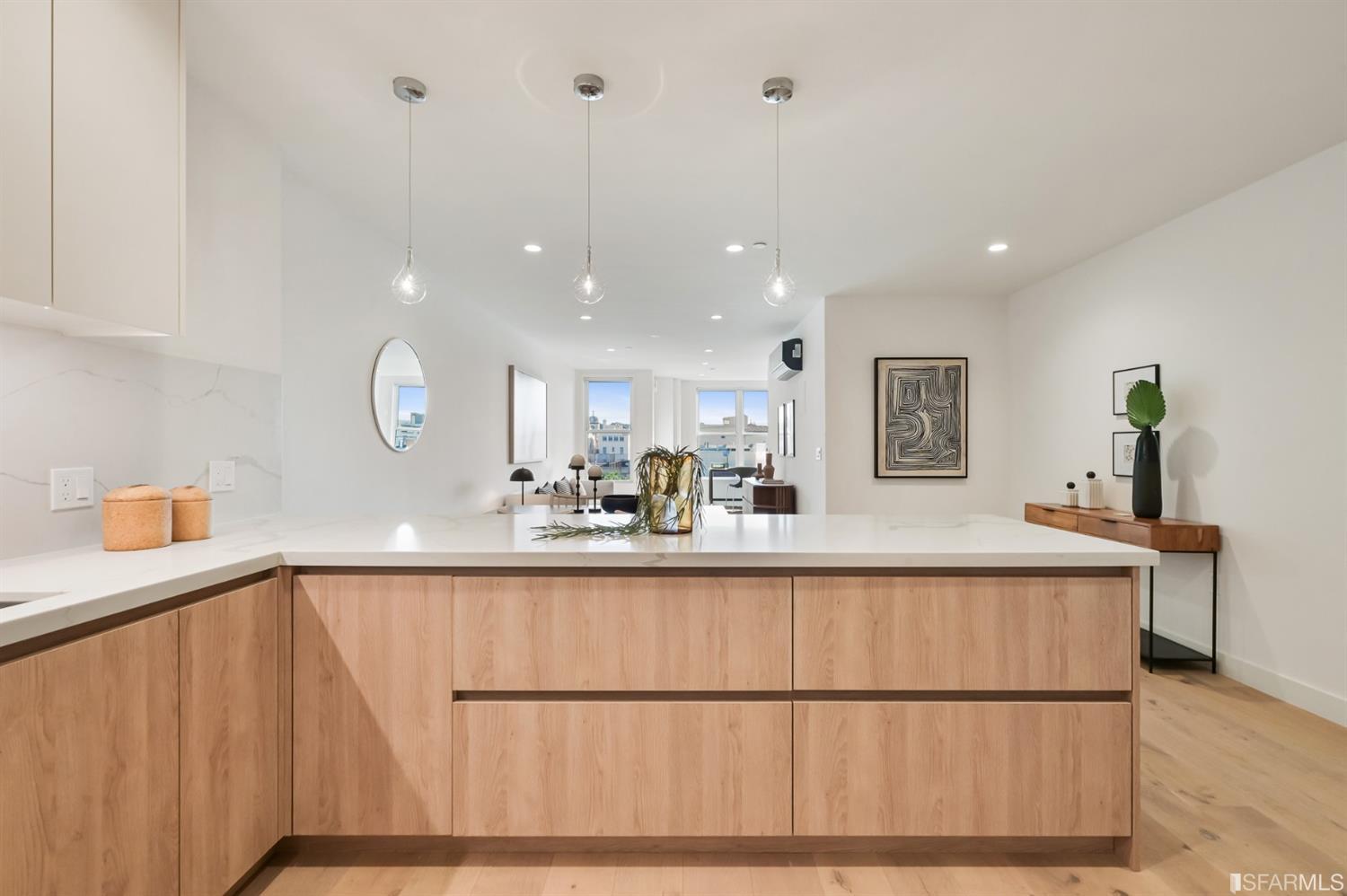 Open-plan kitchen with a light-wood island, white stone countertop, and pendant lights.
