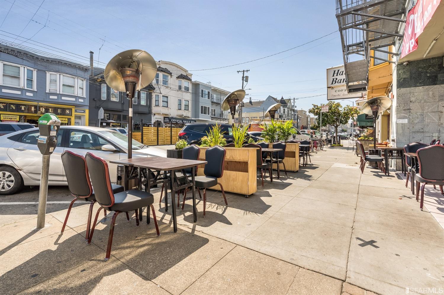 Street scene with sidewalk café seating, storefronts, and parked cars.