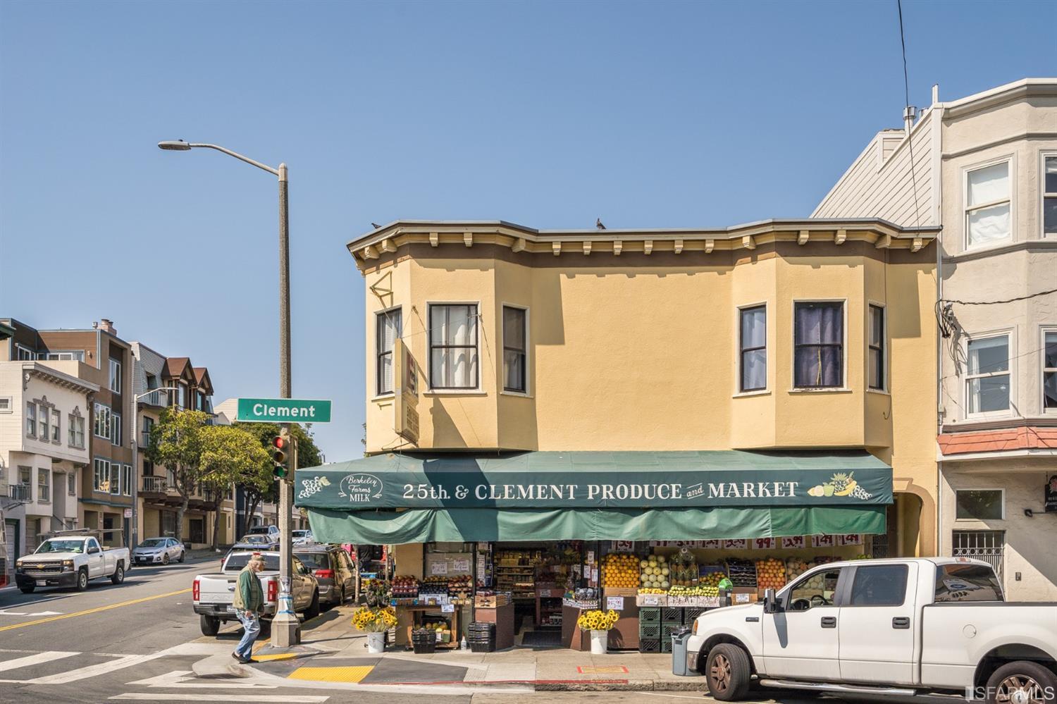 Yellow corner building with a ground-floor produce market beneath a green awning at Clement Street.