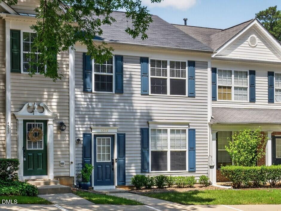 Two-story townhouse with blue shutters, a dark green front door, and trimmed hedges.