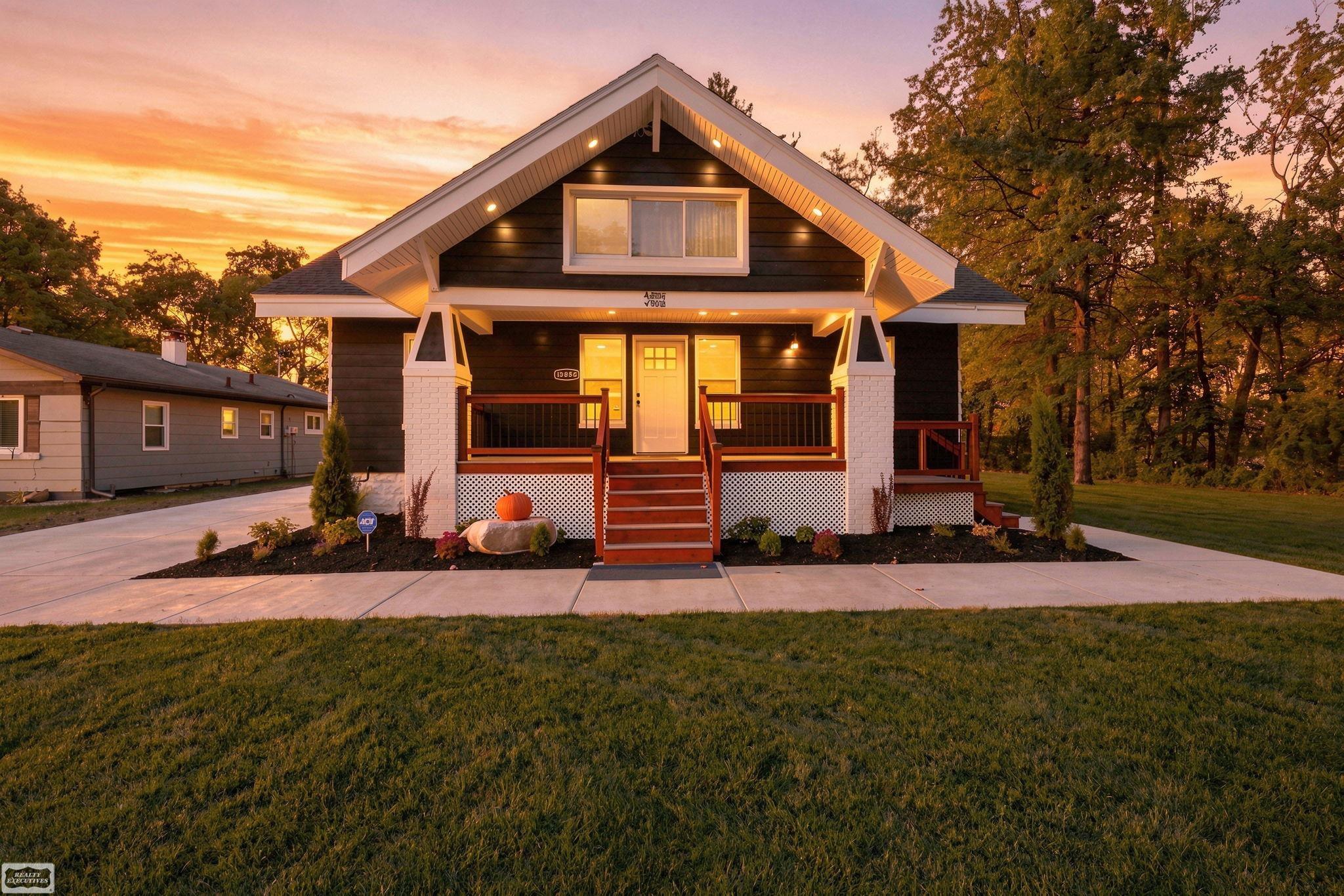 Dark-sided house with a white-trimmed gabled roof and covered porch at sunset.
