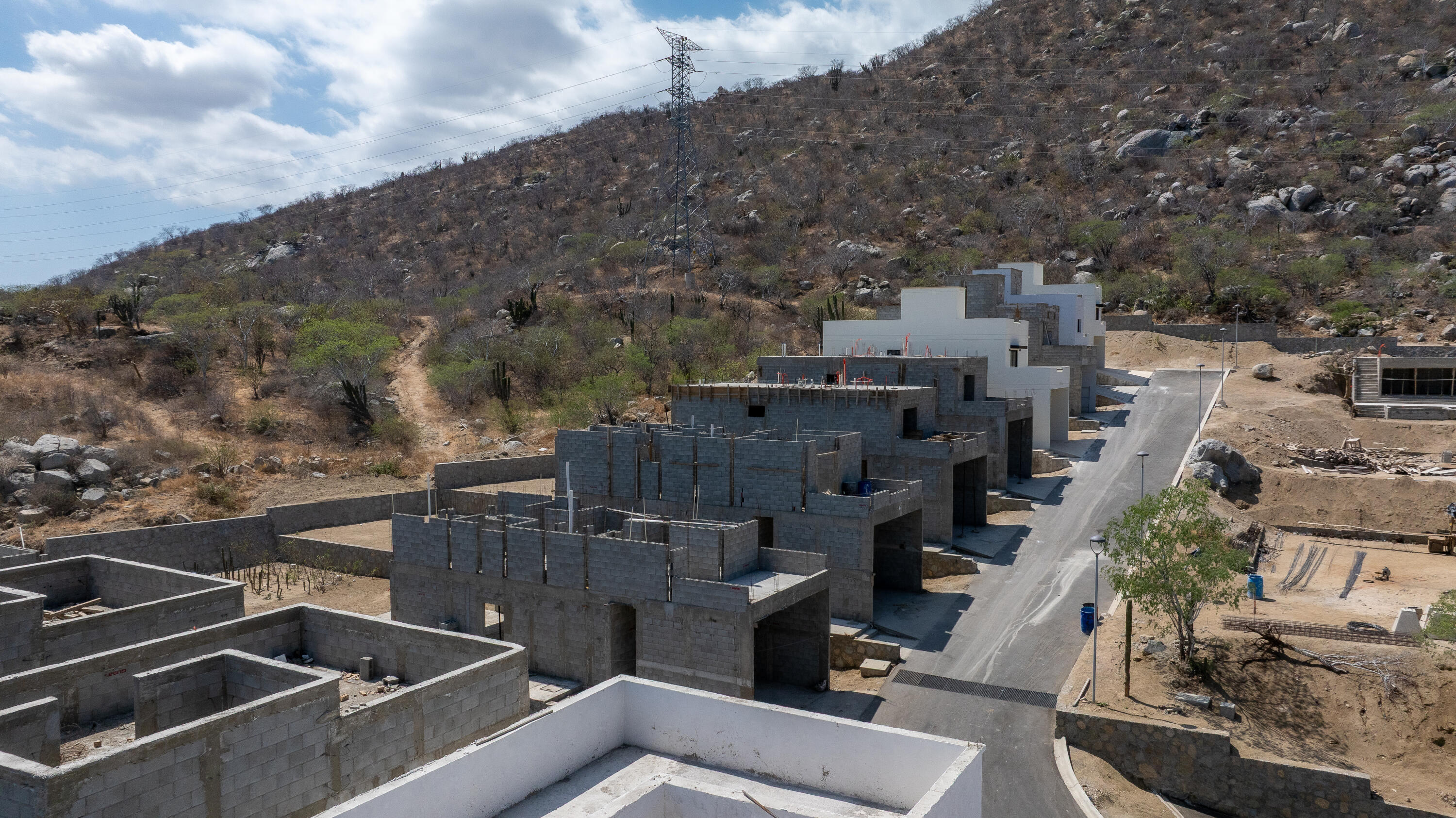 Unfinished hillside homes of gray block beside a paved road and rocky, cactus-dotted slope.