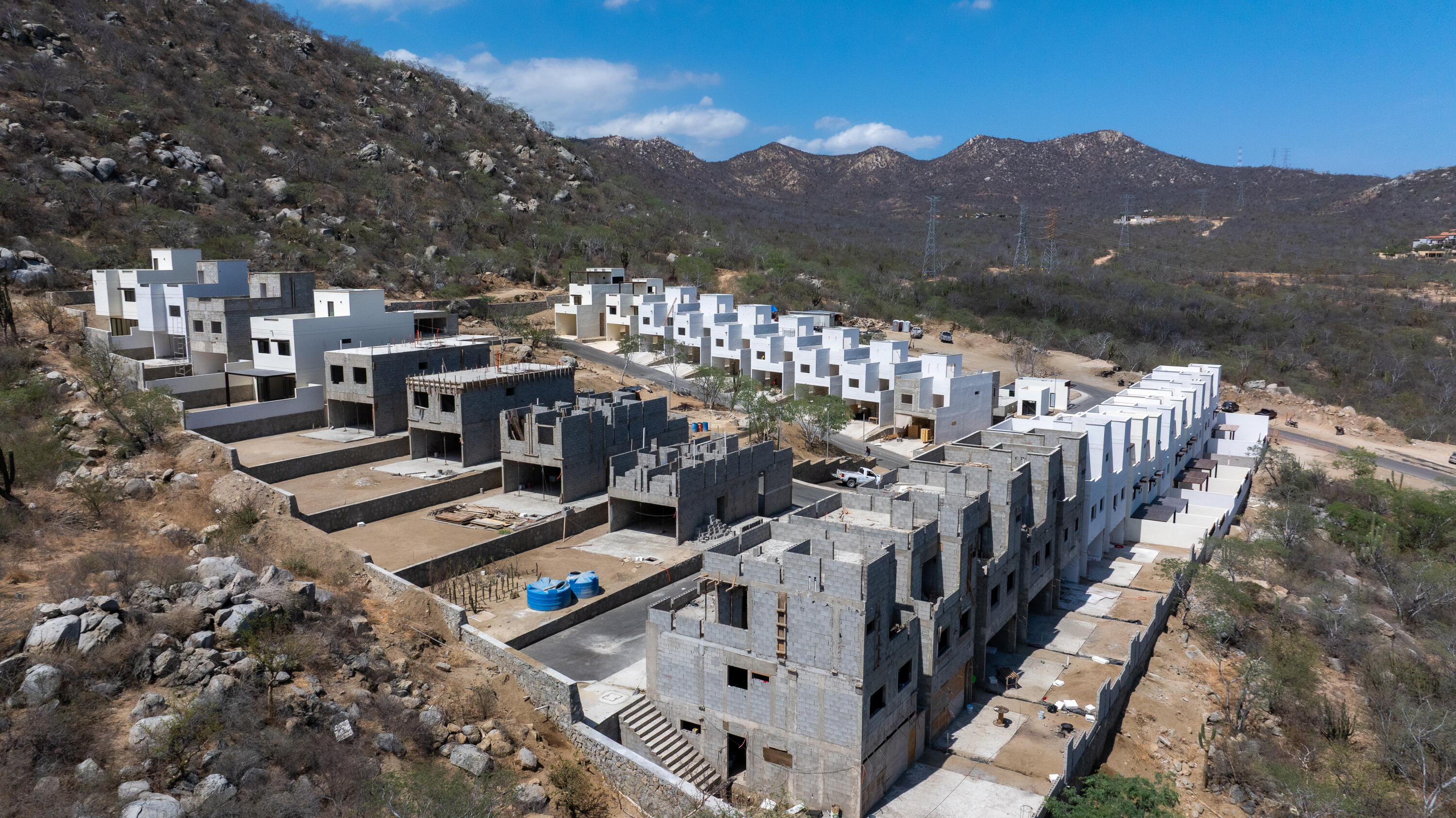 Aerial view of modern homes under construction among dry, rocky hills.