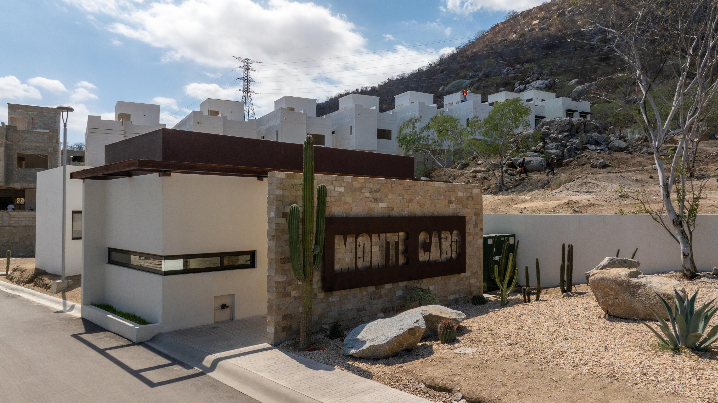 Monte Cabo community entrance with a stone sign, modern white buildings, and desert landscaping.
