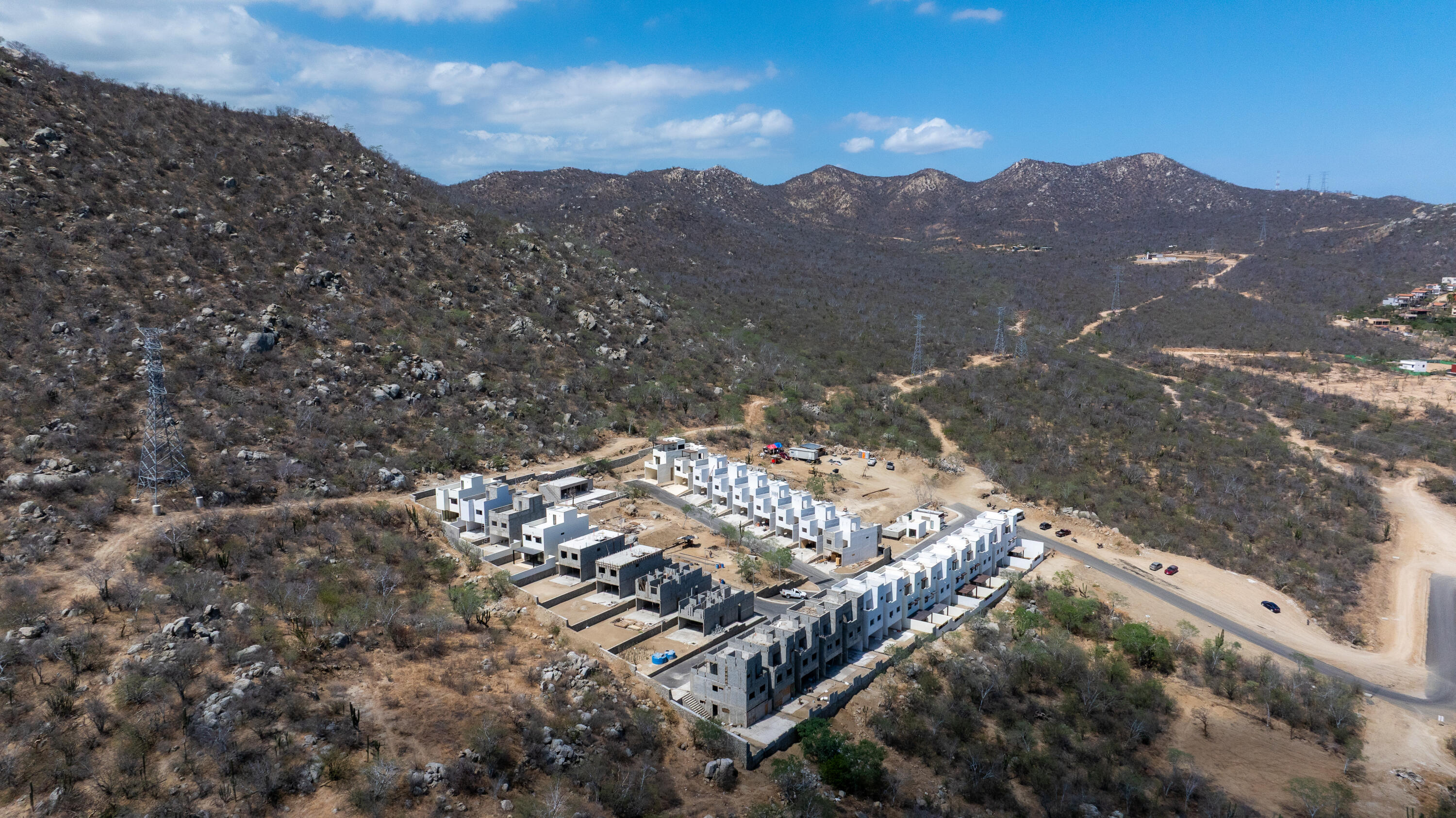 Aerial view of modern homes under construction among dry, rocky hills.