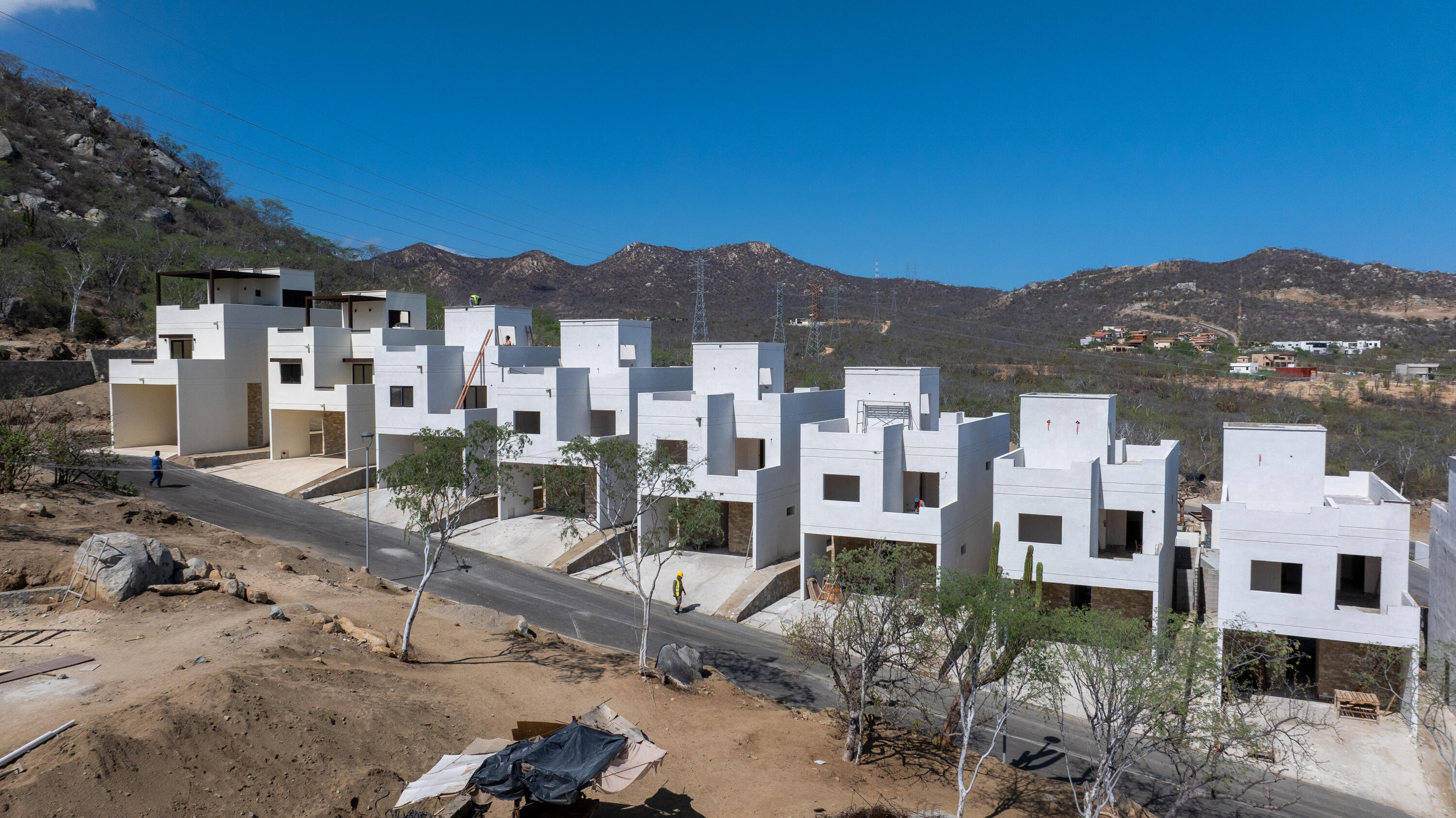 Row of modern white homes under construction beside a paved road, with dry mountains behind them.
