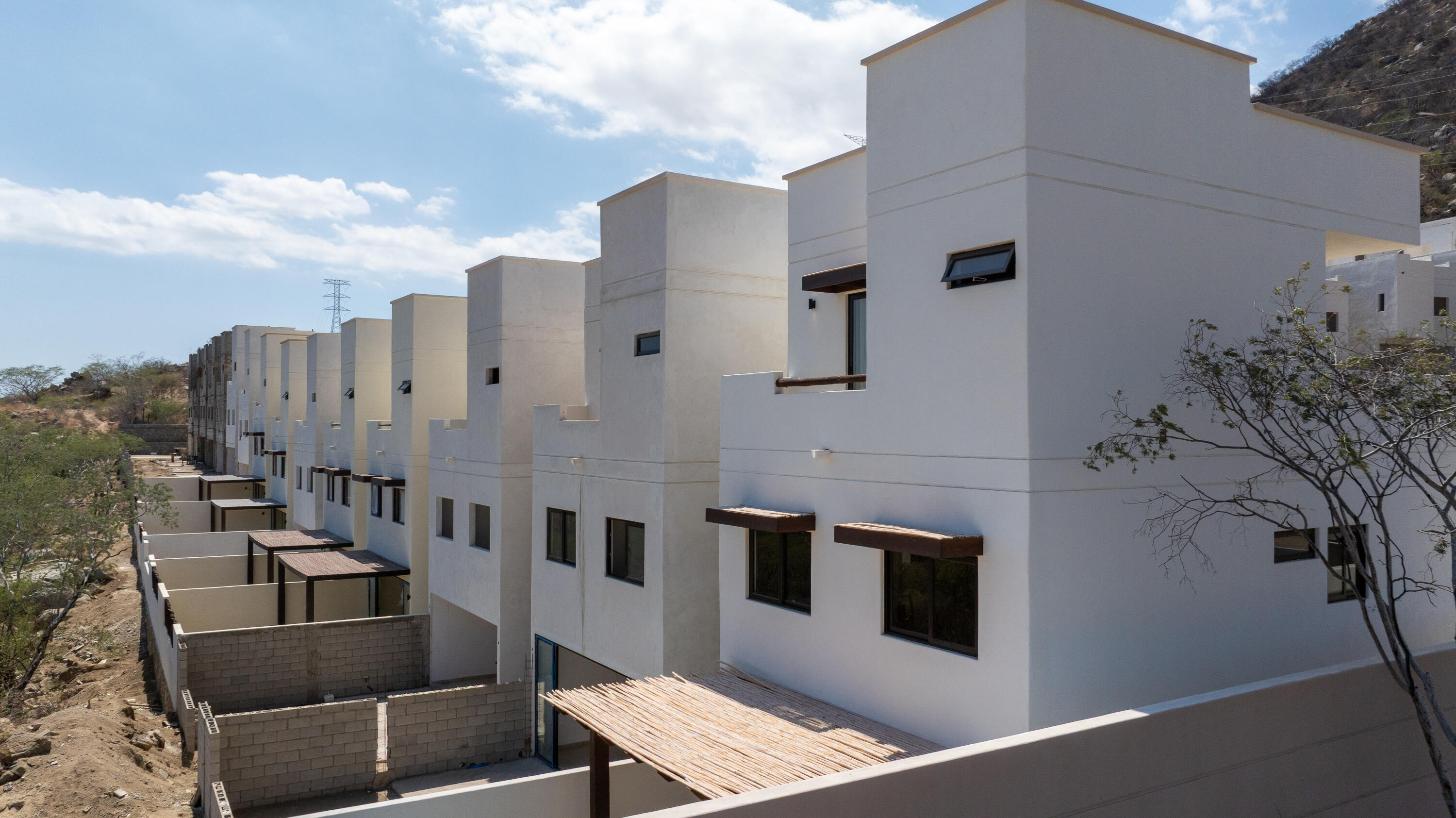 Row of modern white townhouses with dark windows and unfinished courtyard walls.