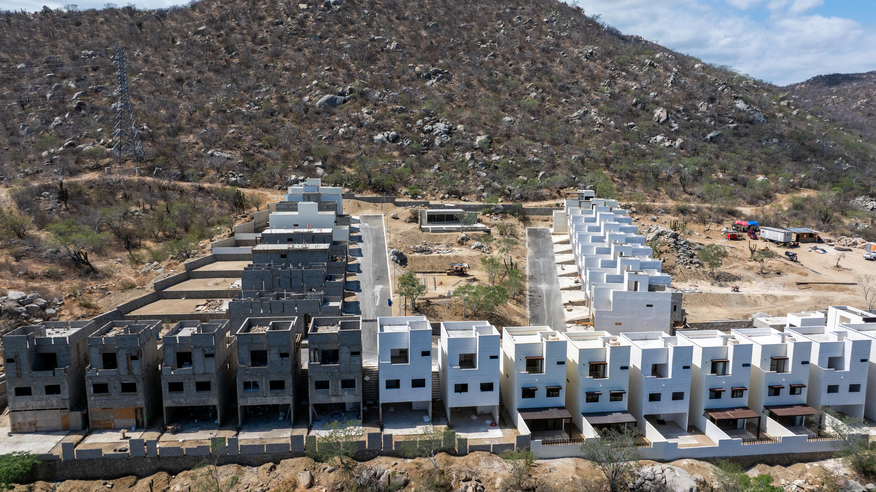 Aerial view of modern townhouses under construction beside a rocky hillside.