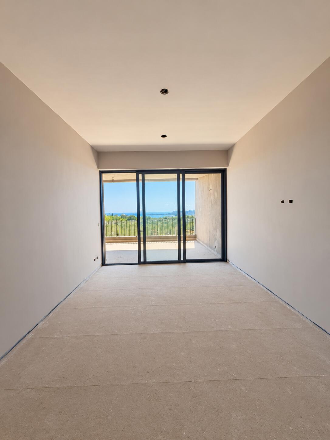 Empty room with stone flooring and sliding glass doors opening to a balcony with an ocean view.