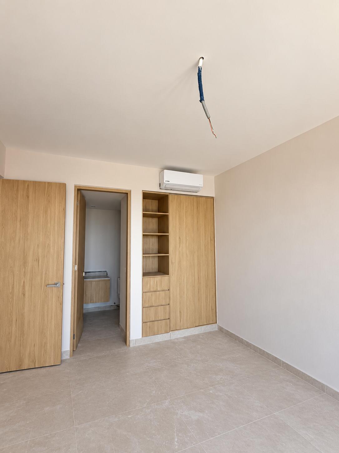 Empty bedroom with built-in wood cabinetry, wall-mounted air conditioner, and an exposed ceiling wire.