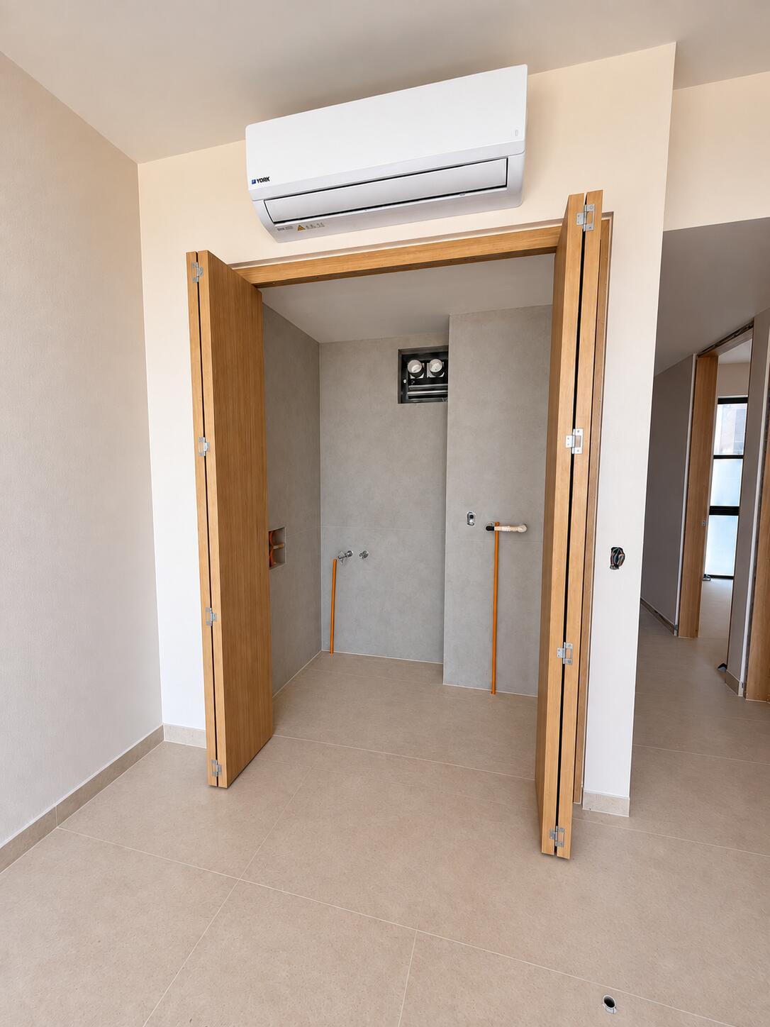 Unfinished shower enclosure with open wooden doors and a wall-mounted air conditioner.
