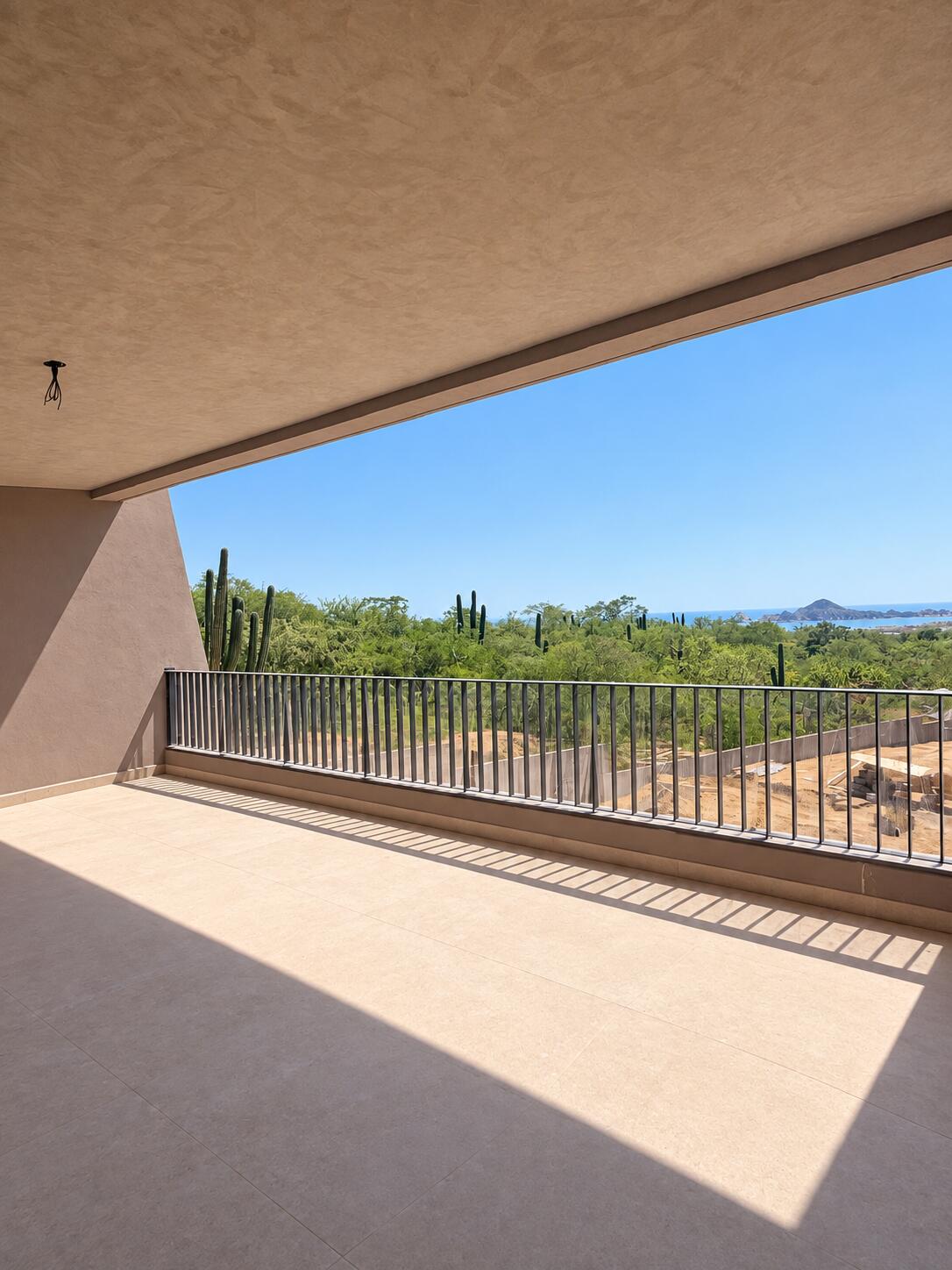 Covered tiled balcony overlooking cacti, desert greenery, and a distant ocean headland.