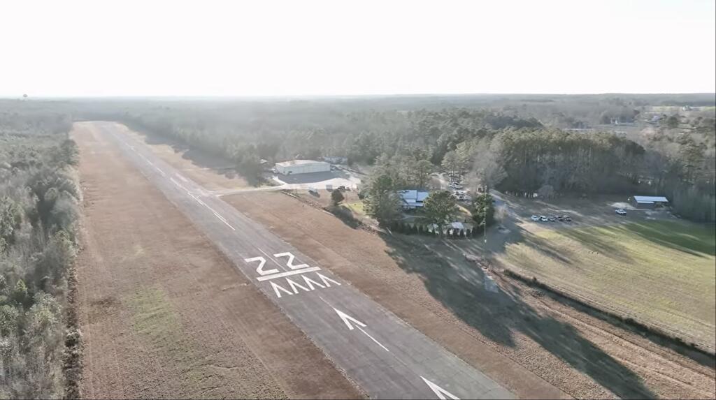 Aerial view of a rural runway marked 22, with hangars and surrounding wooded land.